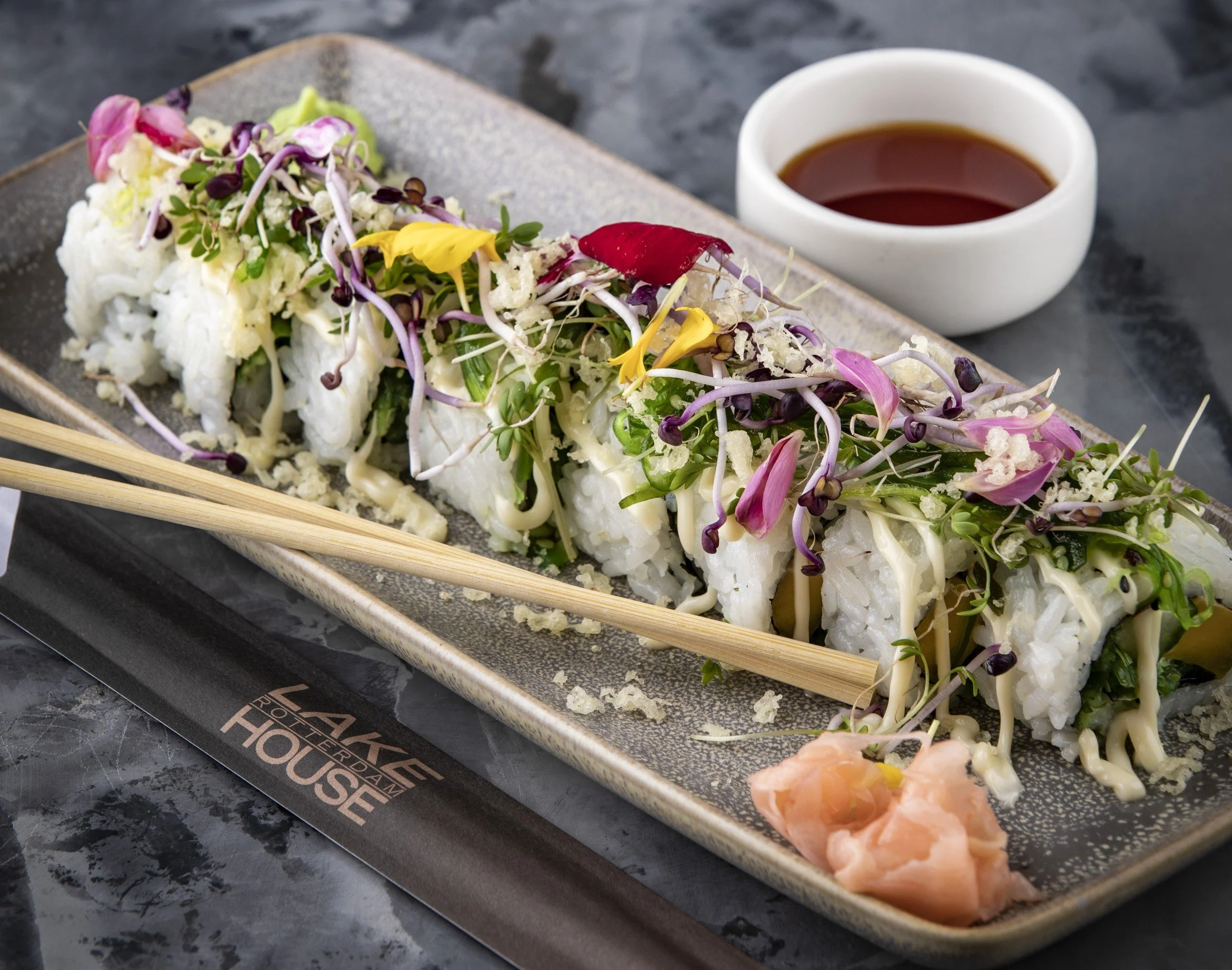 Sushirol met witte rijst, versgebakken groenten en microgreens, geserveerd met sojasaus en gerookte zalm op een keramisch bord