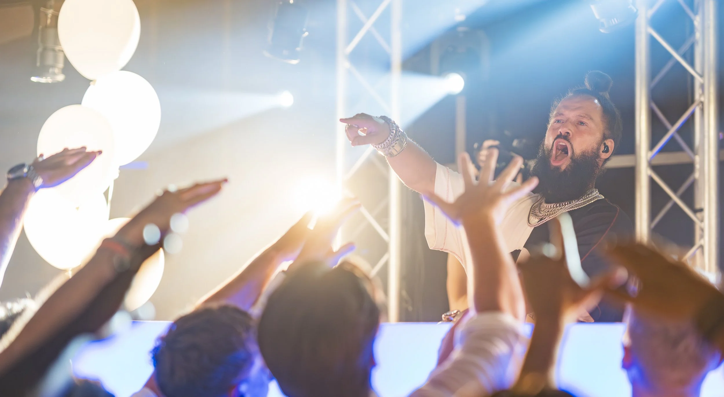 Man met een beugel op de tong en sieraden viert feest met de menigte tijdens een concert of evenement, onder kleurrijke lichten.
