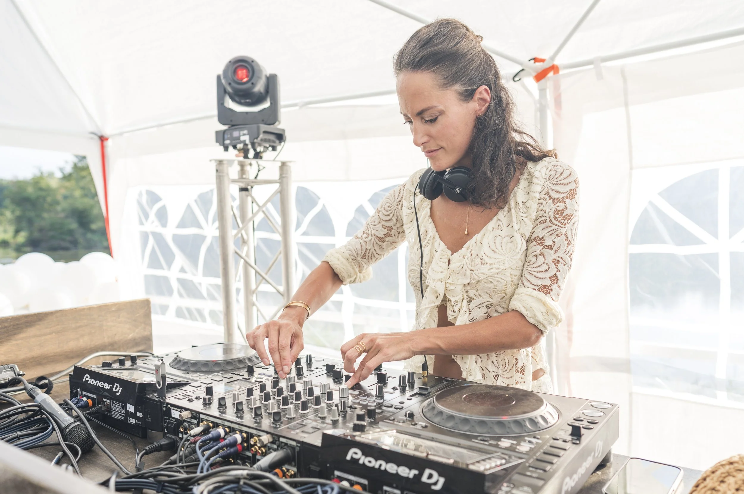 Vrouw die een DJ-controller bedient onder een witte tent, met professionele koptelefoon om haar nek.