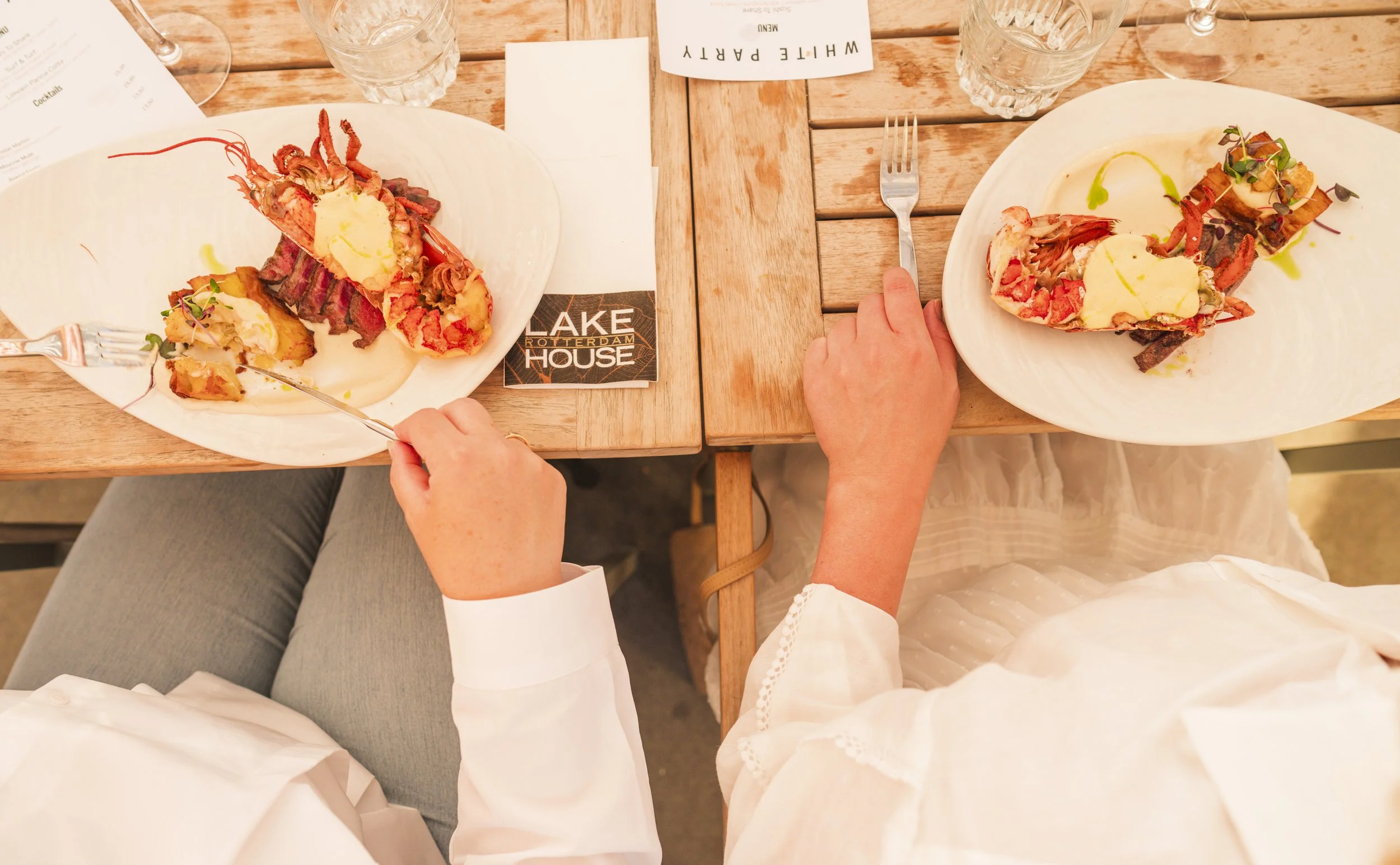 Cephalopod met boter en microgreens op een wit bord, zijde- of knoflookfrietjes, op houten tafel met water en een menu op de achtergrond.
