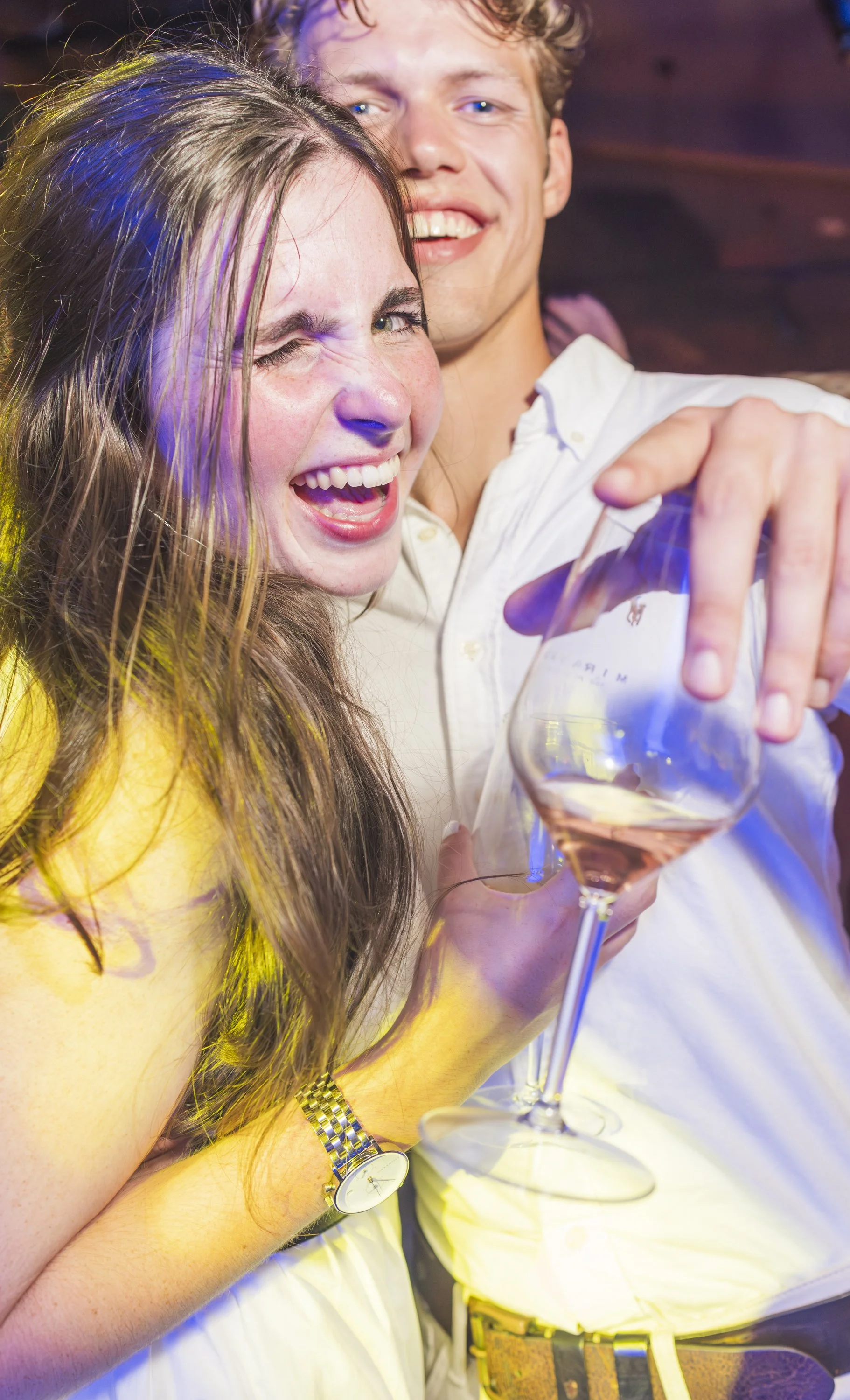 Twee vrolijke jonge mensen die een feestje vieren, een meisje met lang haar en een jongen met kort haar, ze lachen en houden een glas rosé wijn vast.