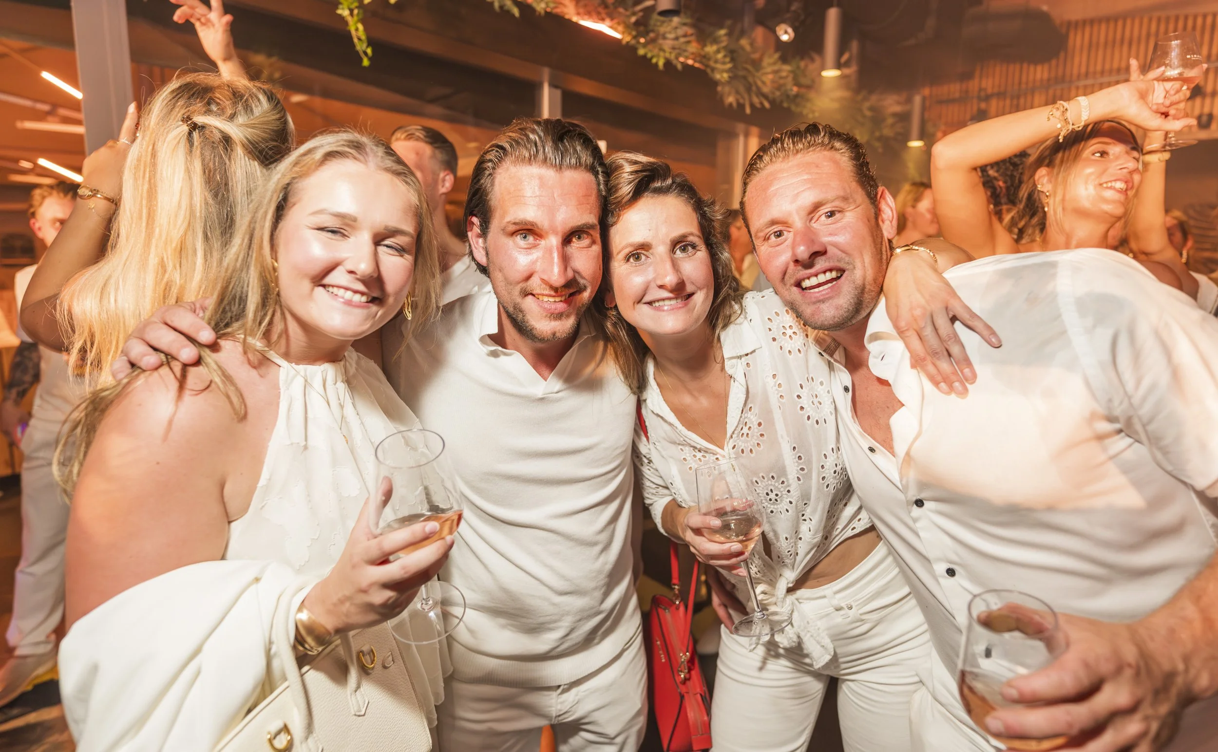 Groep mensen die samen feest vieren, glimlachend en in een gezellige sfeer, met glazen wijn in de hand.
