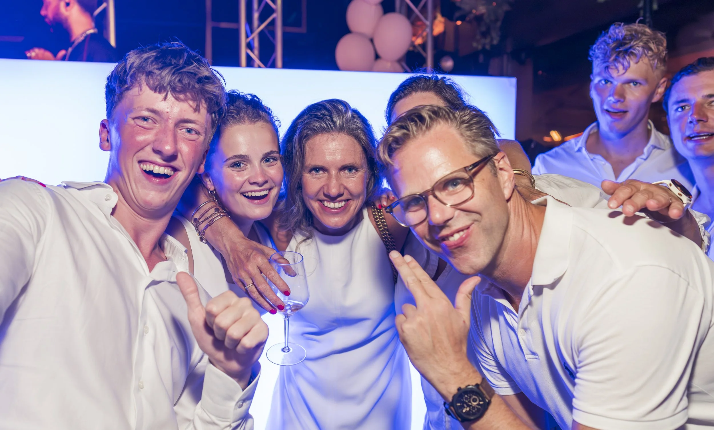 Groep mensen die samen lachen en plezier hebben op een feestje, met balloons en lichteffecten op de achtergrond.