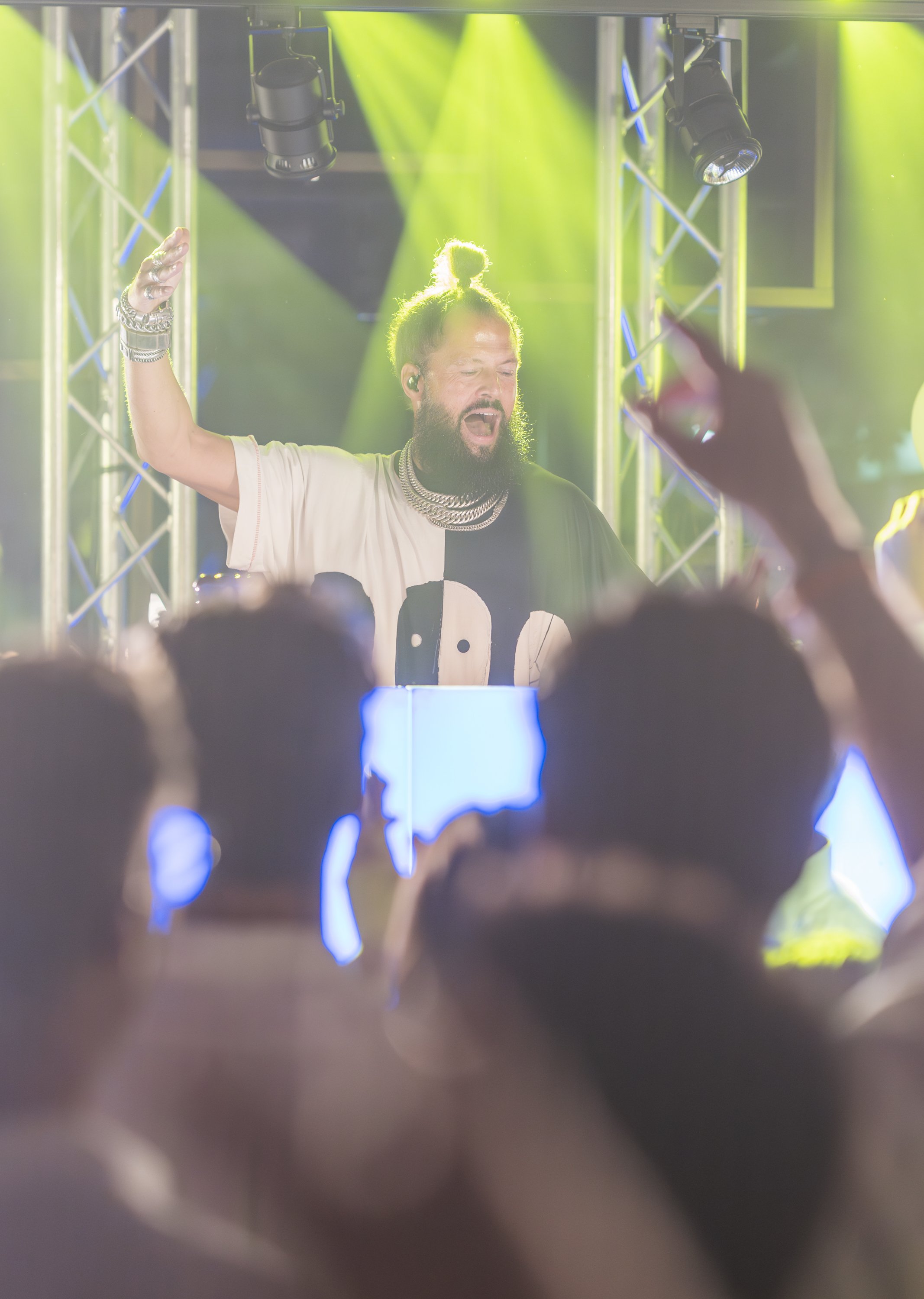 Een man met een pet in een DJ-set met groene en gele lichtstralen.
