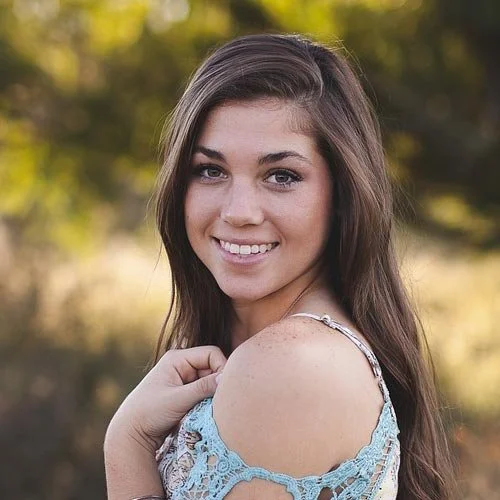Retrato de una joven sonriendo al aire libre con fondo de árboles y luz natural