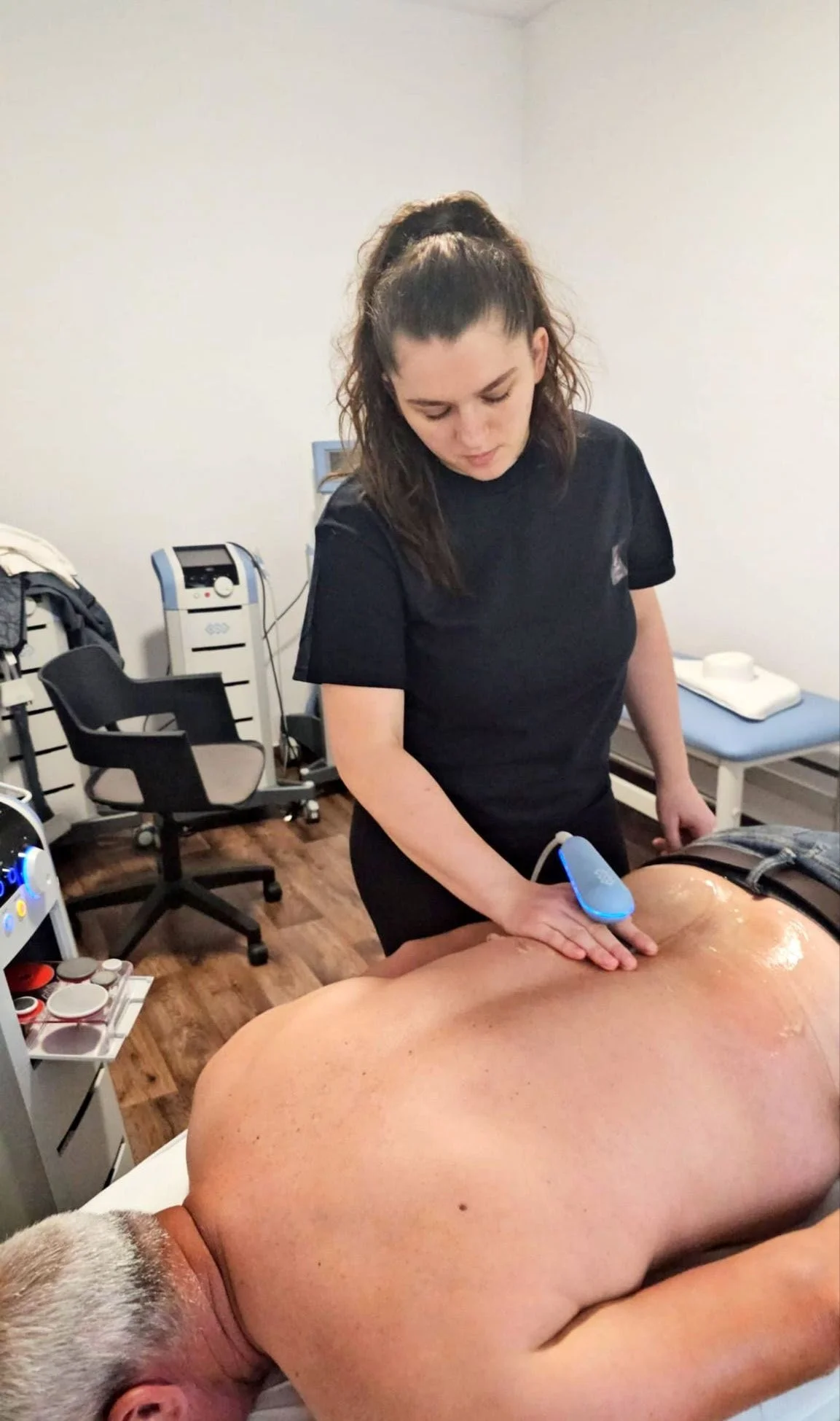 A woman performs a cupping therapy session on a man's back in a medical or therapy room.