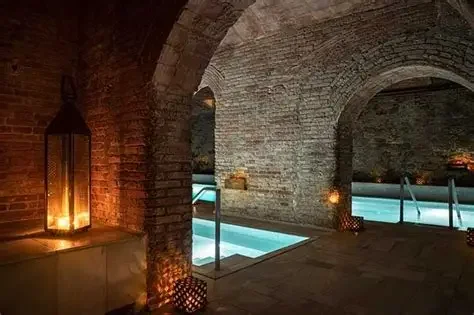 Indoor swimming pool with arched stone ceiling and brick walls, illuminated by ambient lighting and lanterns.