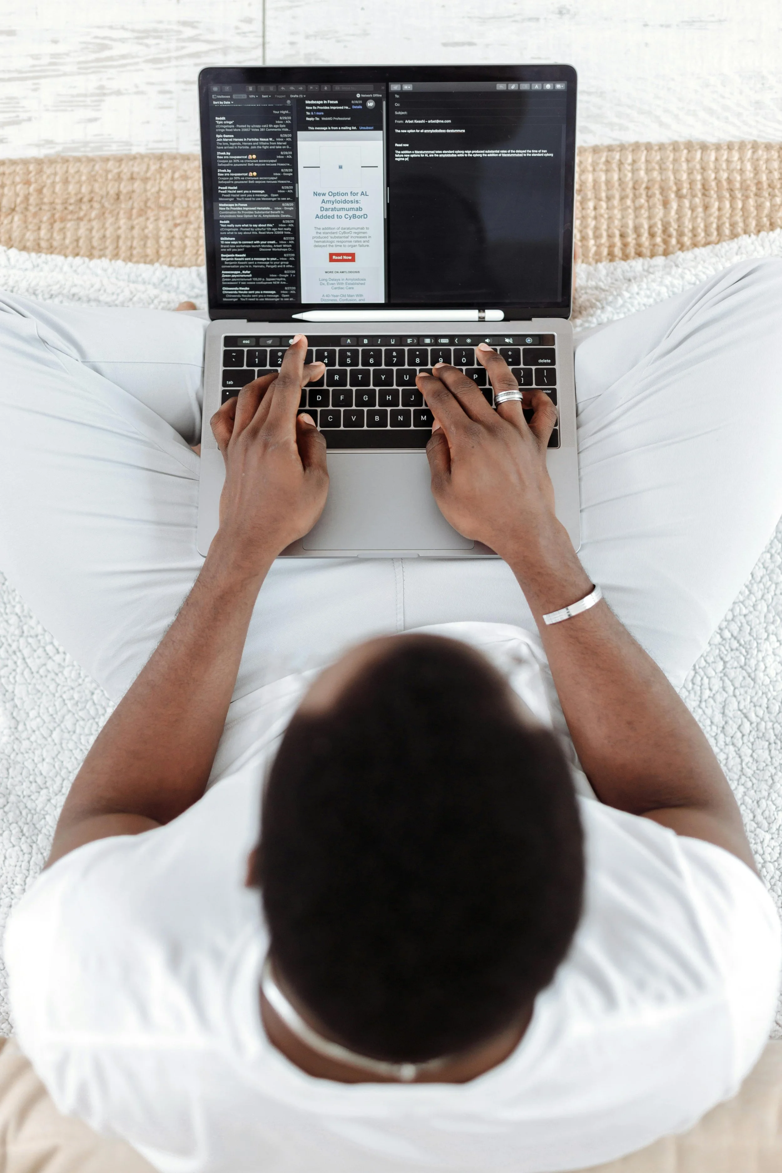 Person sitting cross-legged on a textured white and beige surface, typing on a laptop with an email and article open on the screen.