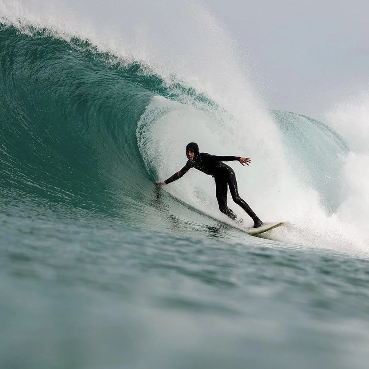 Surfer wearing a wetsuit and helmet riding inside the barrel of a large wave.