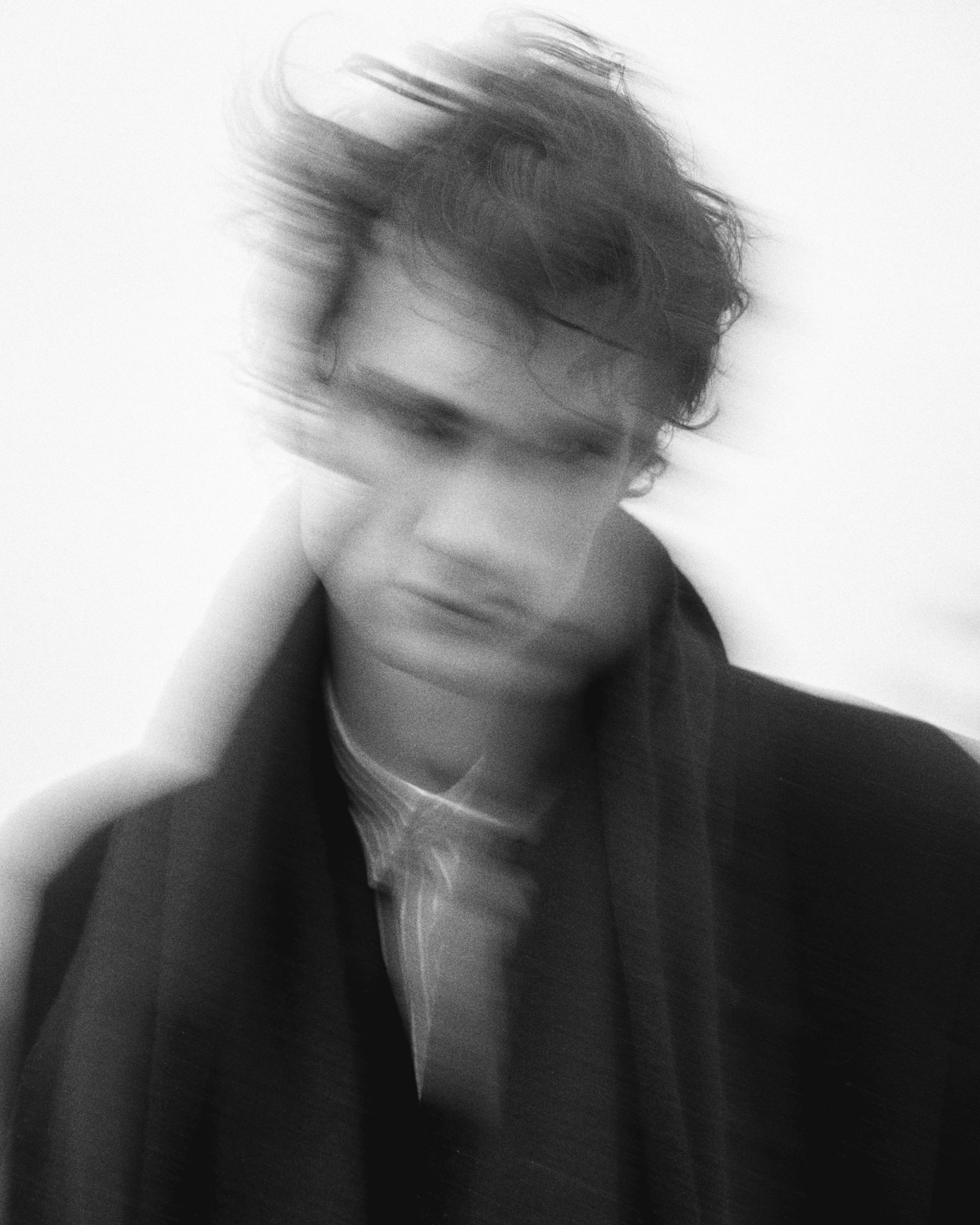 Black and white photo of a person with short, messy hair, slightly turned, wearing earphones and a striped shirt.