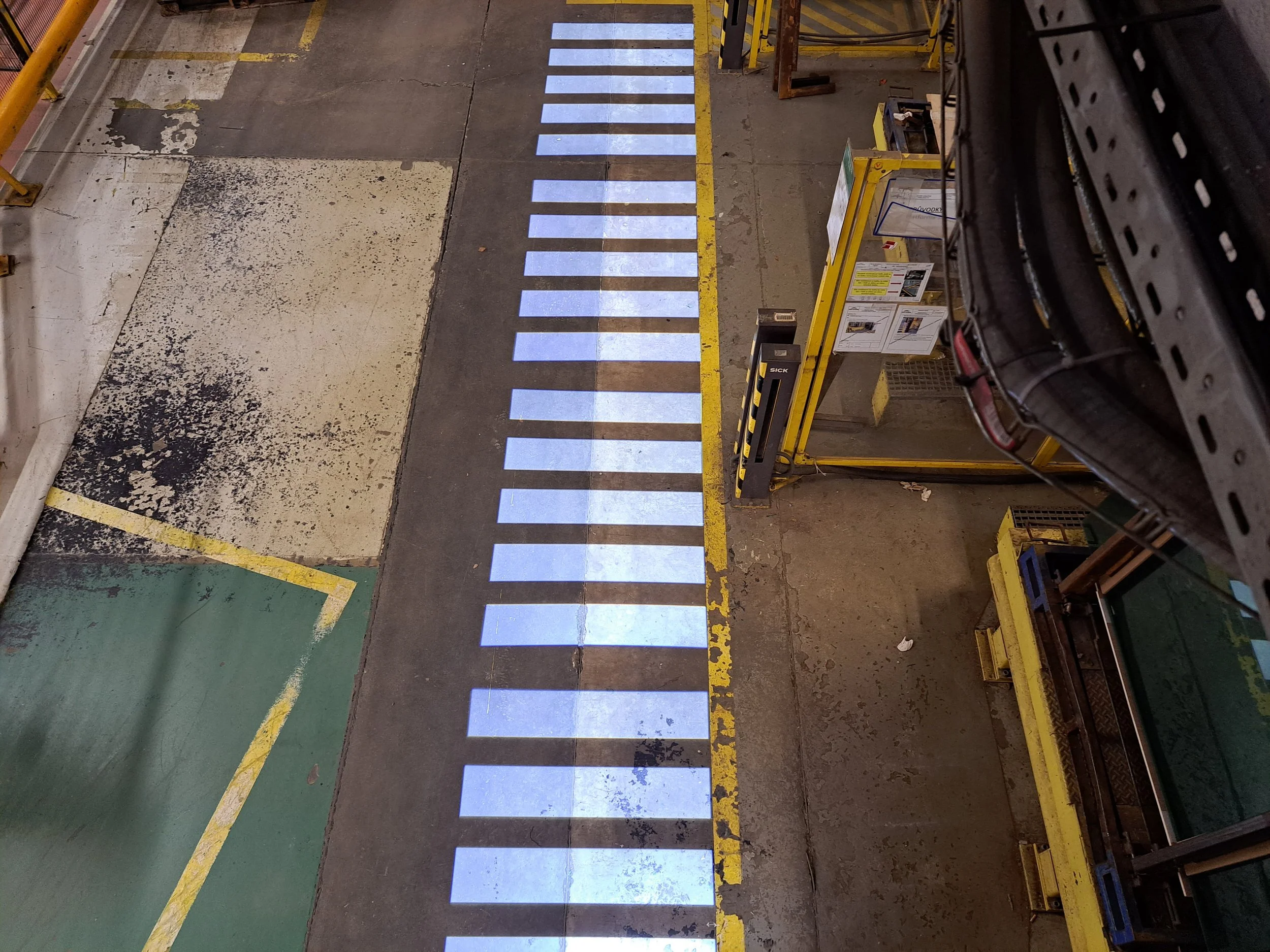 Industrial warehouse floor projected white crosswalk lines and painted yellow safety markings.