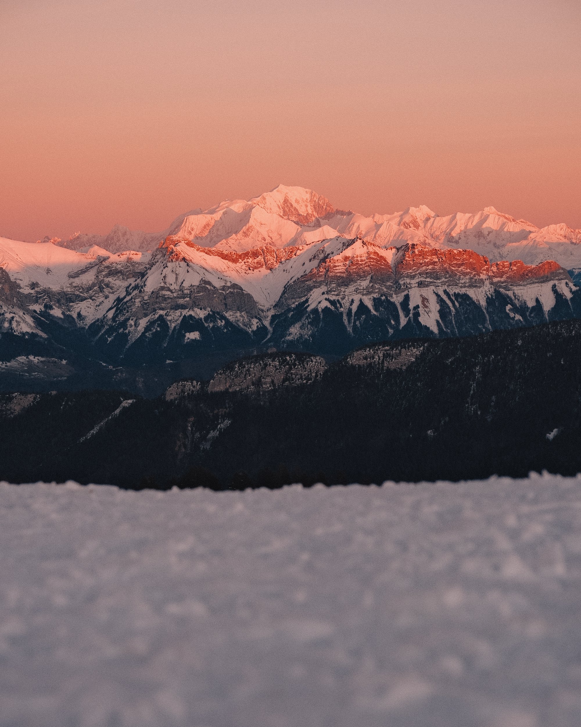 Coucher de soleil sur des montagnes enneigées, avec un ciel rose pâle. Paysages, photo, montagne, rando, randonnée, sport, outdoor, exposition