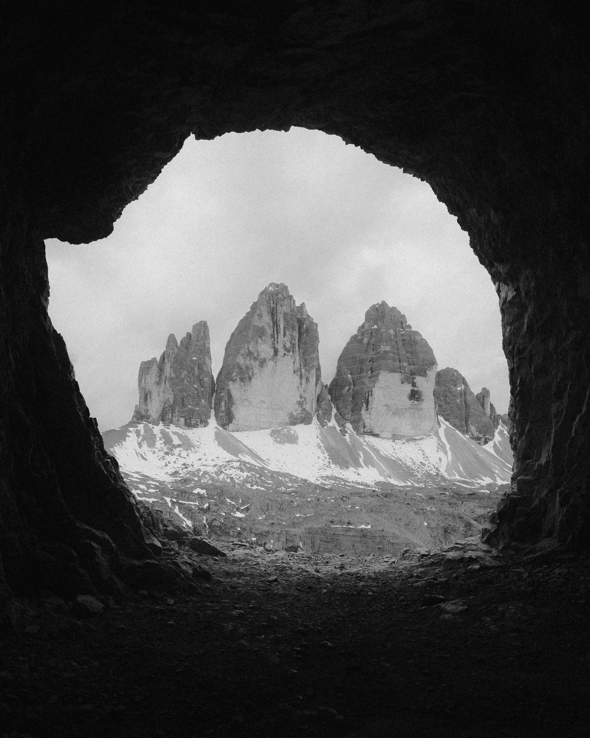 Paysage montagneux vu d'une grotte, avec trois grands rochers enneigés en arrière-plan, en noir et blanc. Paysages, photo, montagne, rando, randonnée, sport, outdoor, exposition