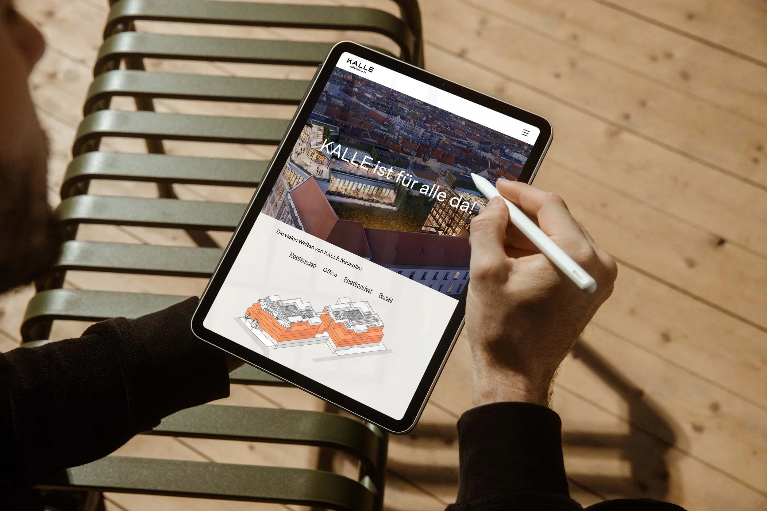 Person holding a tablet with a digital design of a building complex on a wooden bench