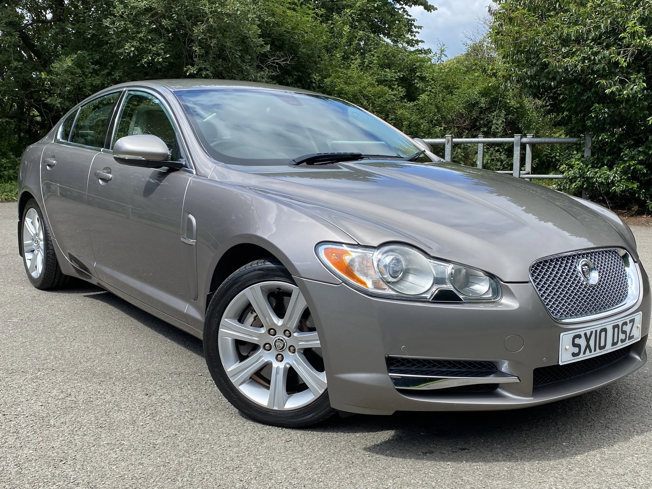 A silver Jaguar X-Type sedan parked outdoors on a paved surface with green bushes in the background.
