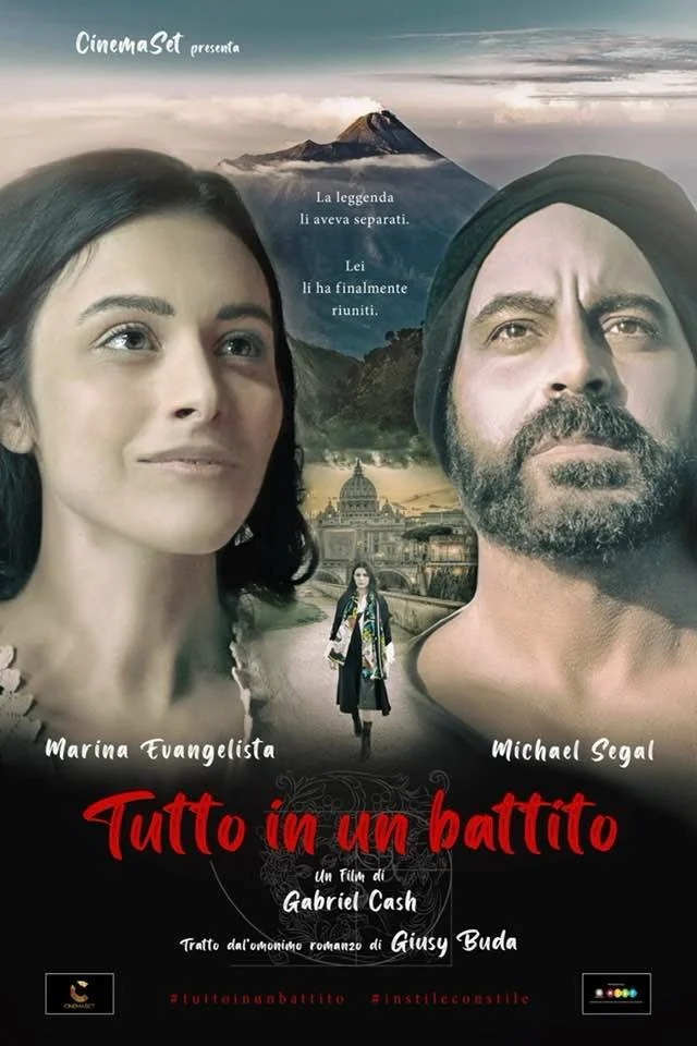 Poster di un film intitolato 'Tutto in un battito'. Mostra due volti, una donna a sinistra e un uomo a destra, con un paesaggio di montagne e un edificio storico sullo sfondo. Al centro, una donna cammina verso la città.