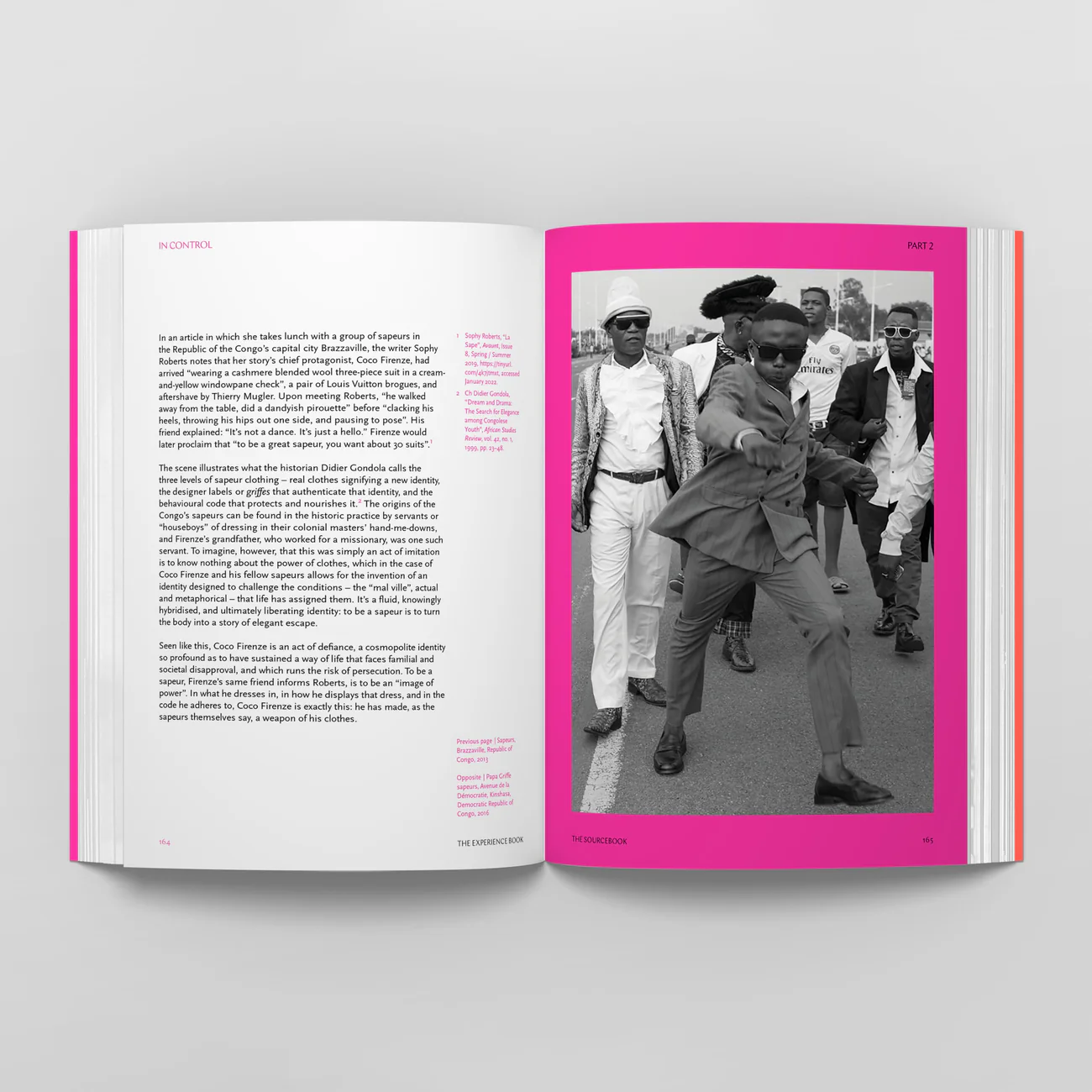 Black and white photo of a group of fashionably dressed people walking on the street, with one person prominently in the foreground dancing or striking a pose, wearing sunglasses and a hat, surrounded by others in stylish clothing.