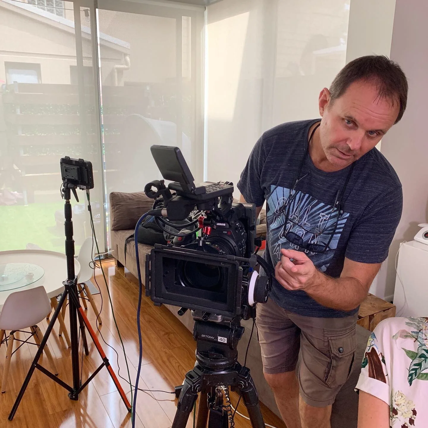 A man operating a professional camera on a tripod inside a room with a glass sliding door.