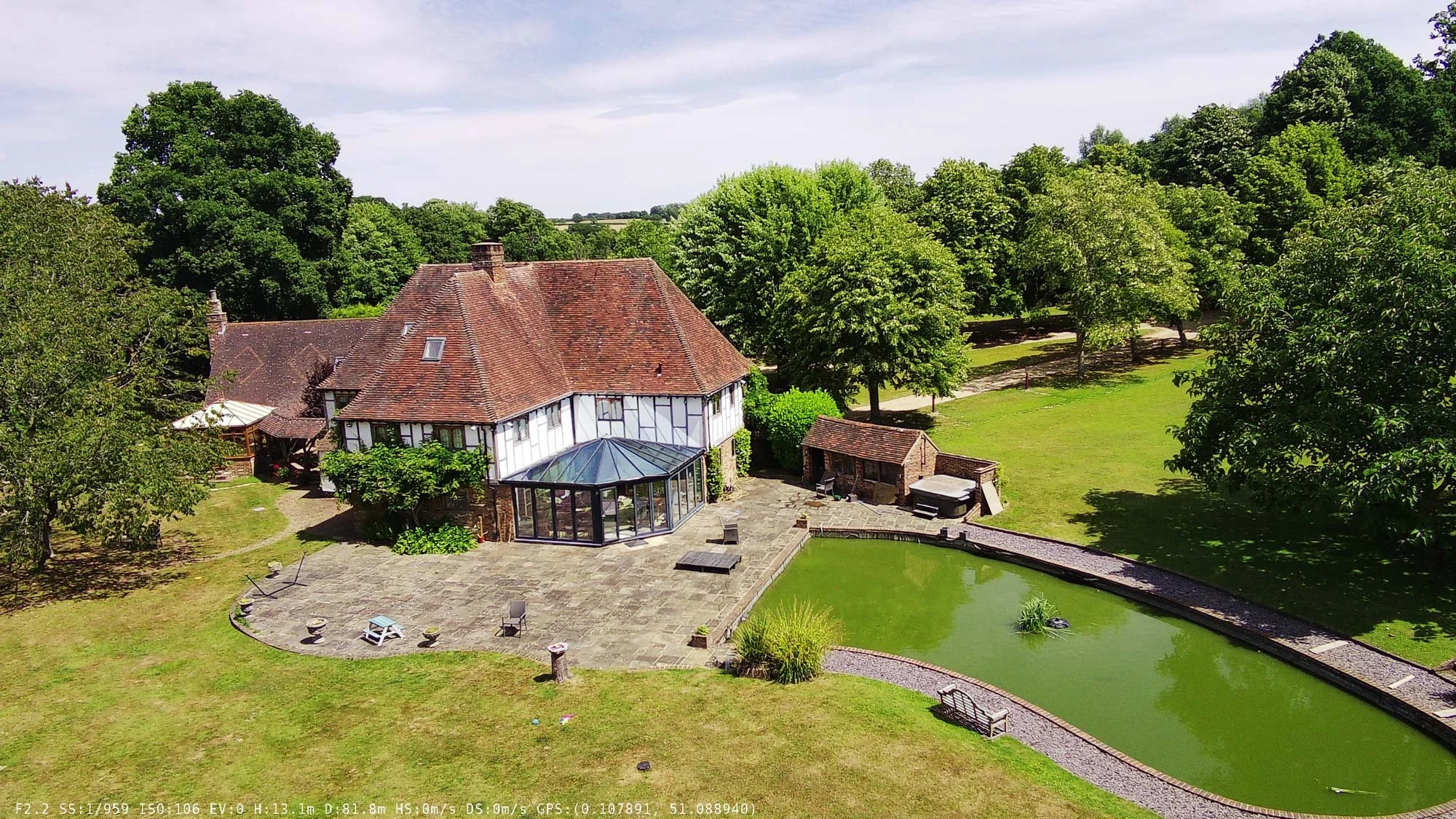 Drone capture of a historic English manor house surrounded by a garden moat and mature trees.