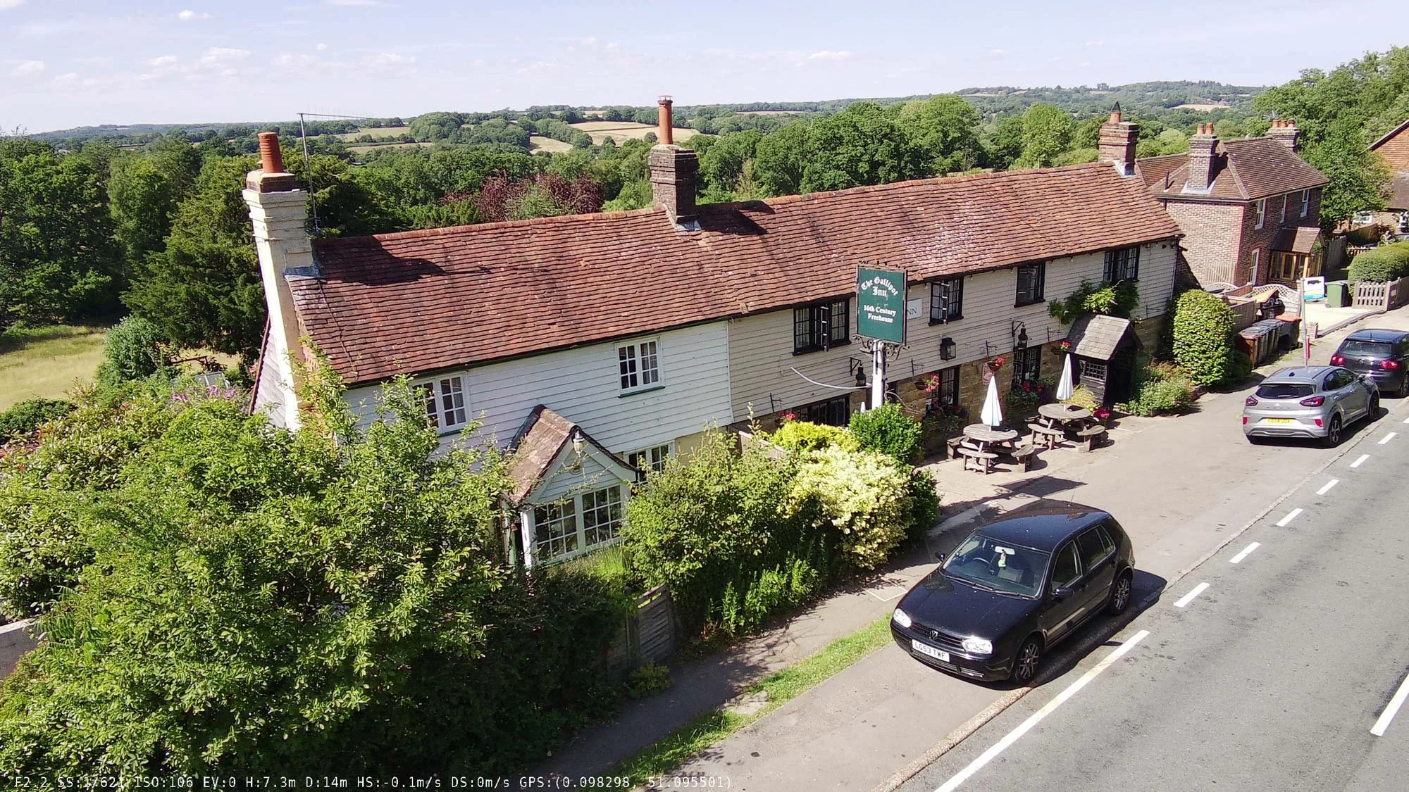Drone image of a row of timber-framed village cottages with red tile roofs and prominent brick chimneys.