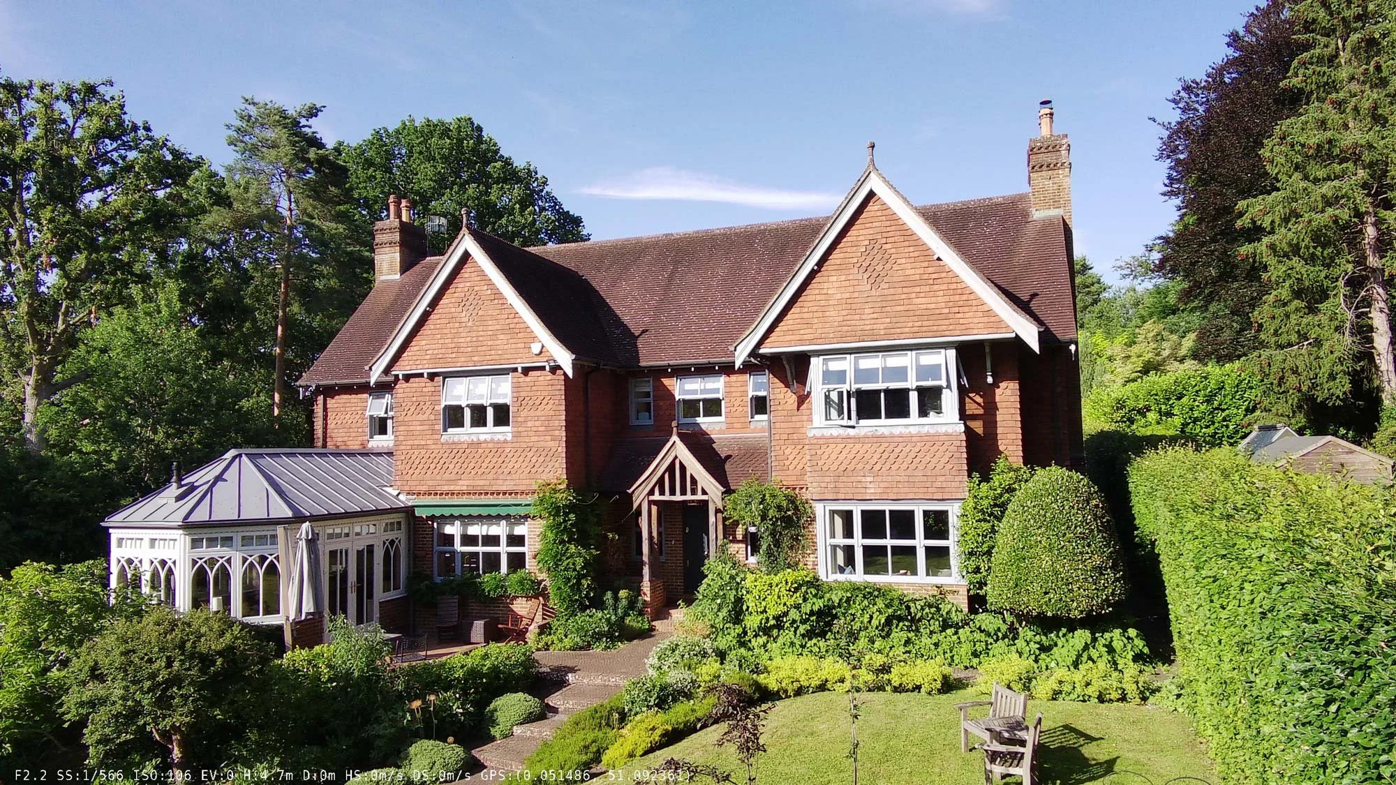 Traditional detached Arts and Crafts style villa with projecting gables, tall chimneys, and manicured hedges.