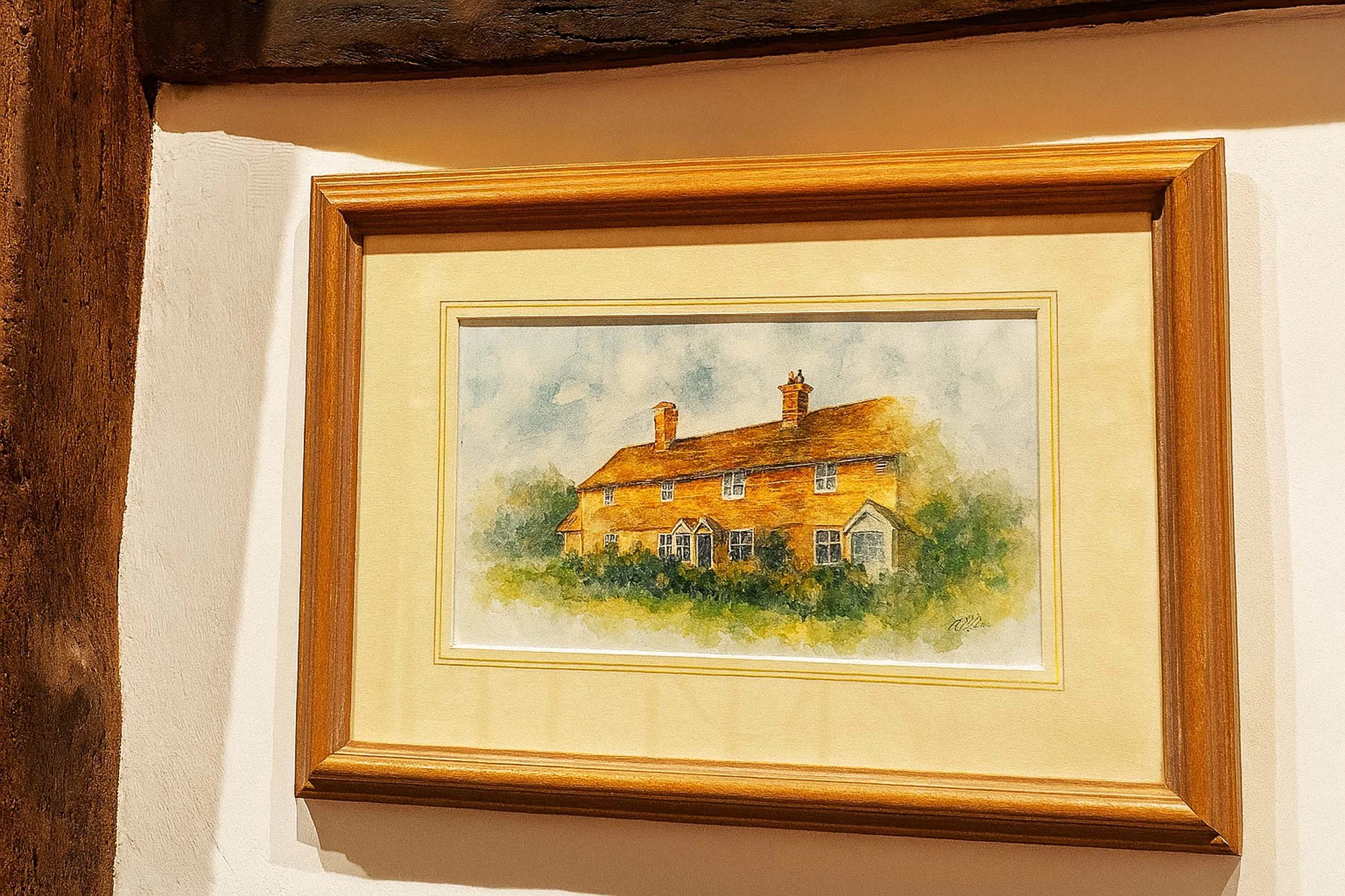 Watercolor painting of a two-story, orange-brown house with multiple chimneys, surrounded by greenery, framed and hanging on a wall.