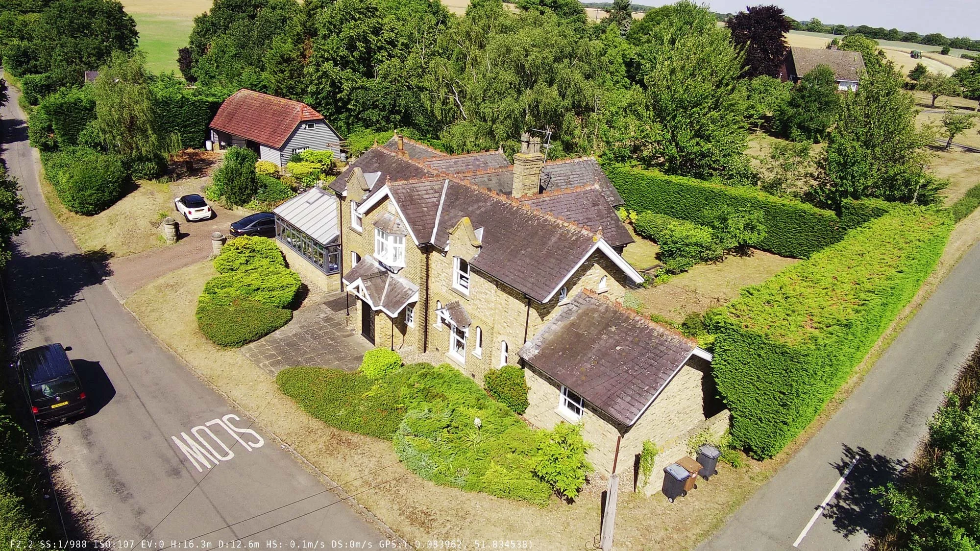 Drone image of a large detached villa in a landscaped neighbourhood with hedges and driveway in front.