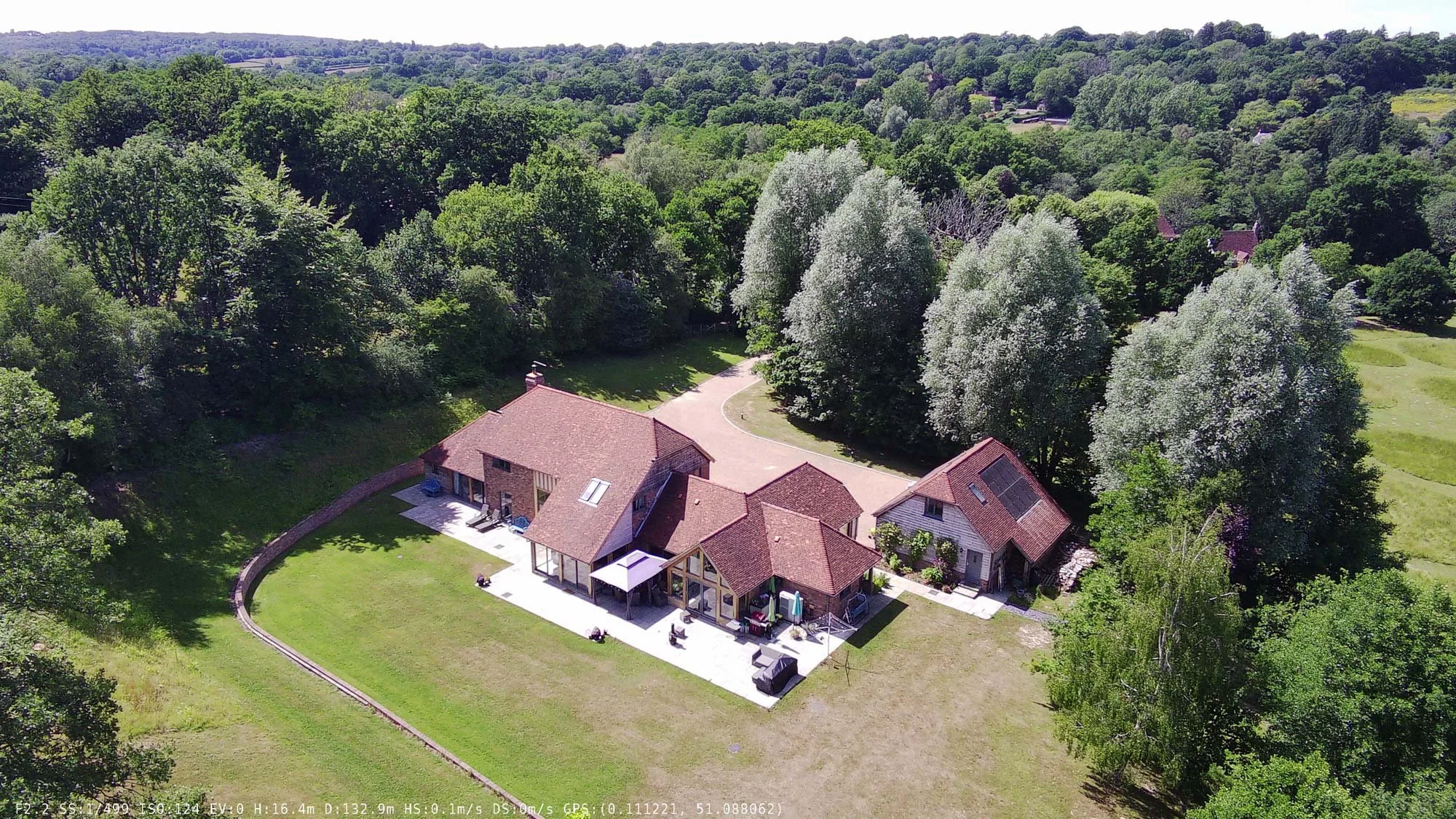 Modern single-storey bungalow complex with large gardens, surrounded by wooded countryside and open lawn.