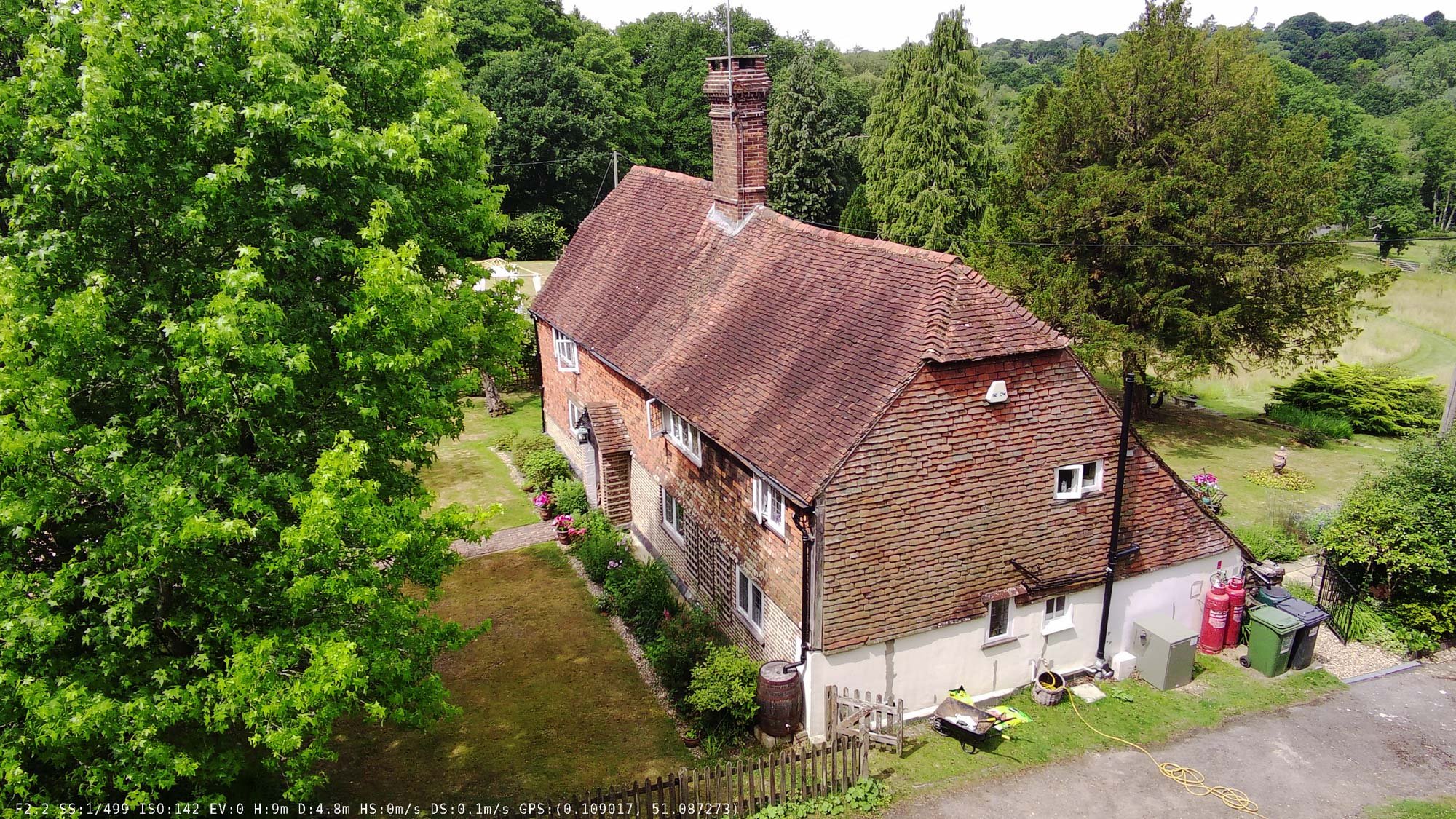 Traditional oak-timbered cottage with steep pitched roof in the English countryside, surrounded by trees.