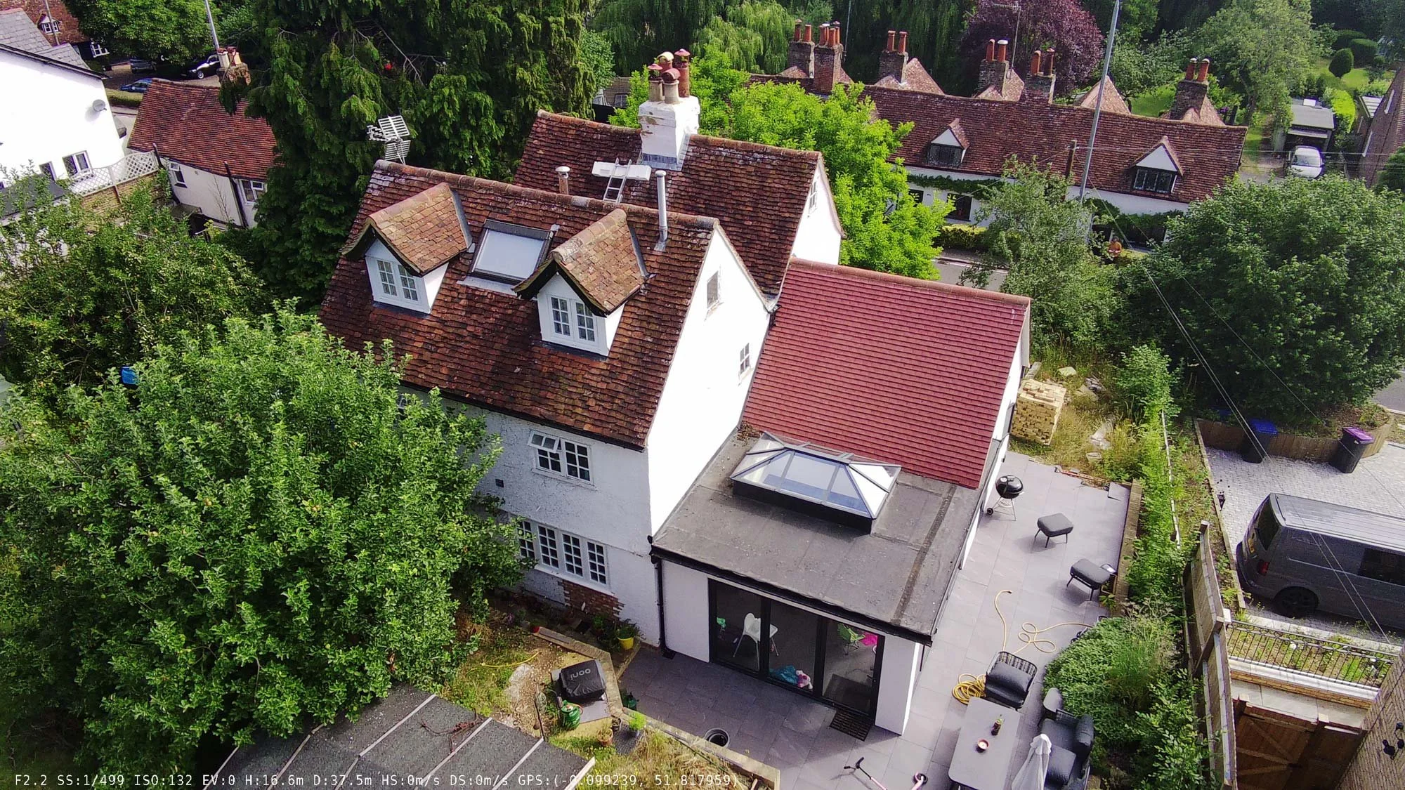 Aerial shot of a whitewashed historic village home with tiled roof, located in a clustered rural English town.