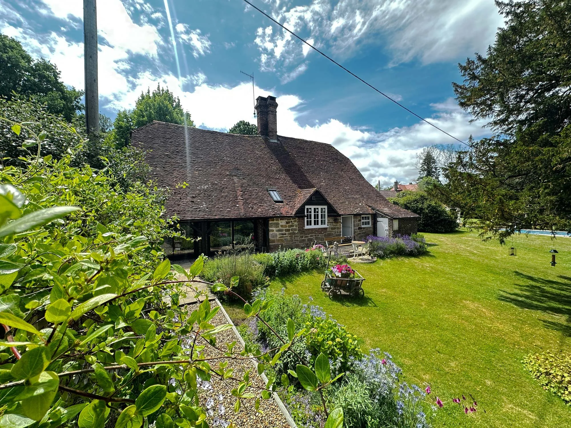 Ground-level photo of a red-brick Arts and Crafts style cottage with lush garden and slate roof.