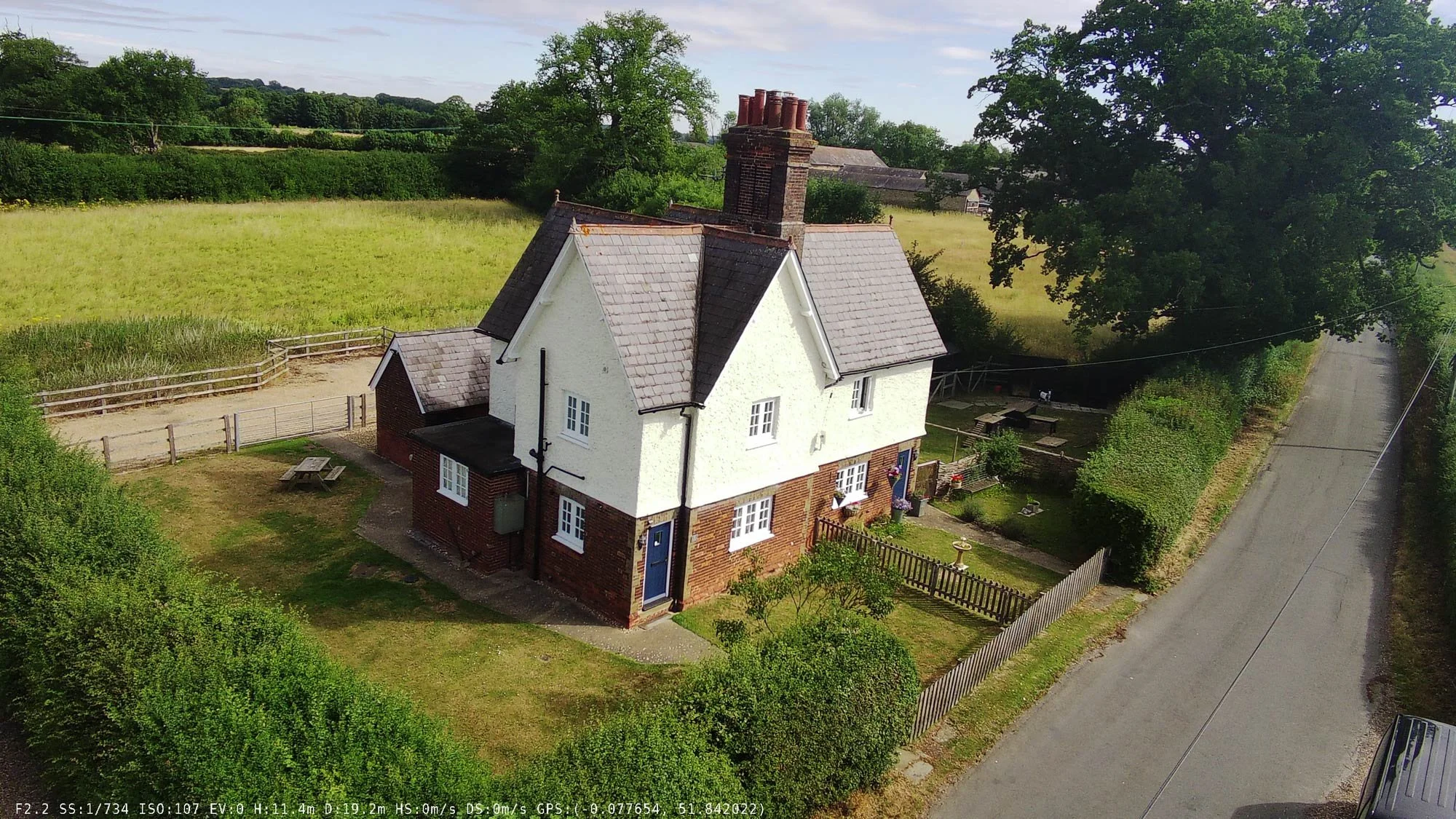 Drone photo of a classic English red-brick cottage surrounded by wheatfields and mature trees.