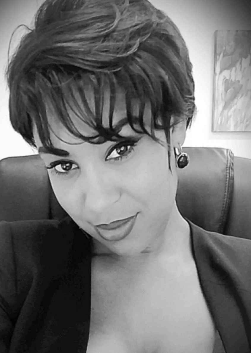 Black and white portrait of Erica Knight, founder of Focus PR Group, with short textured hair, wearing earrings and a blazer, seated in a leather chair, representing leadership in marketing strategy, public relations, and brand consulting.