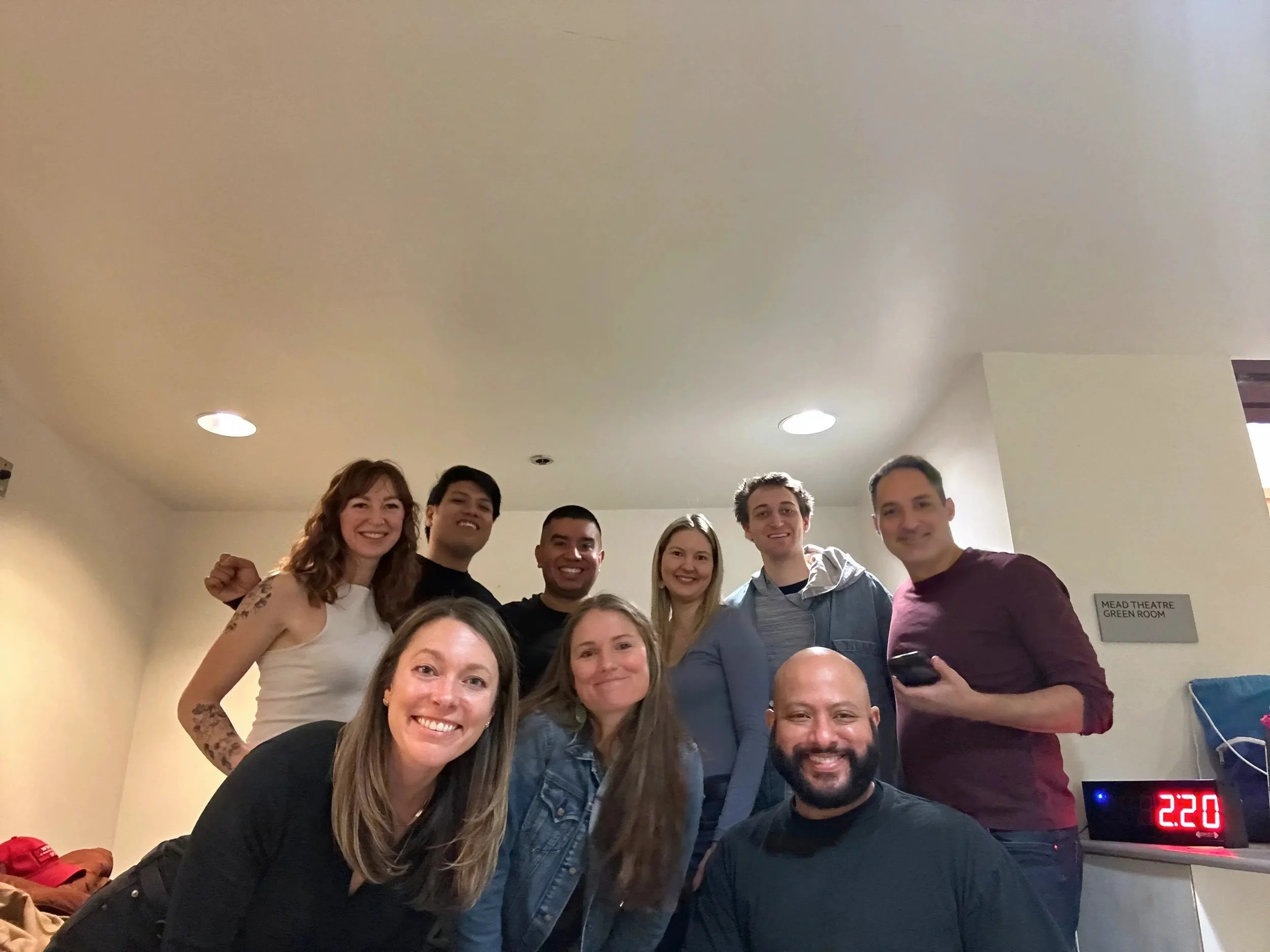 Group of nine people, smiling, gathered indoors for a photo.