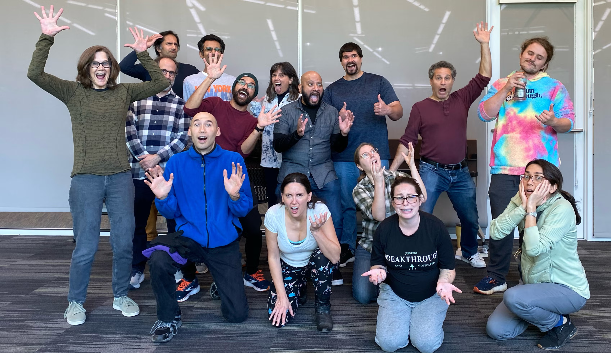 Group of people posing enthusiastically indoors, showcasing a variety of facial expressions and gestures.