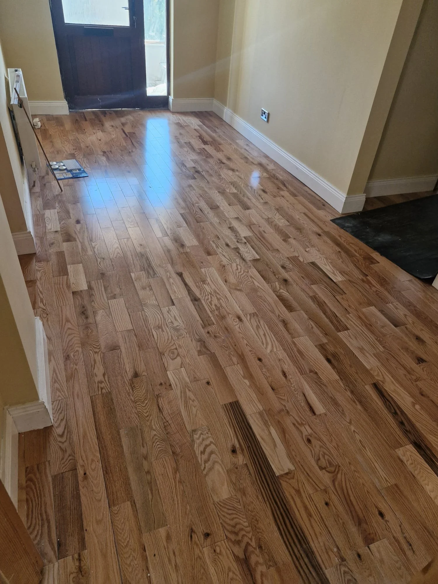 Room with newly installed hardwood flooring, an open door leading outside, and a black mat to the right.
