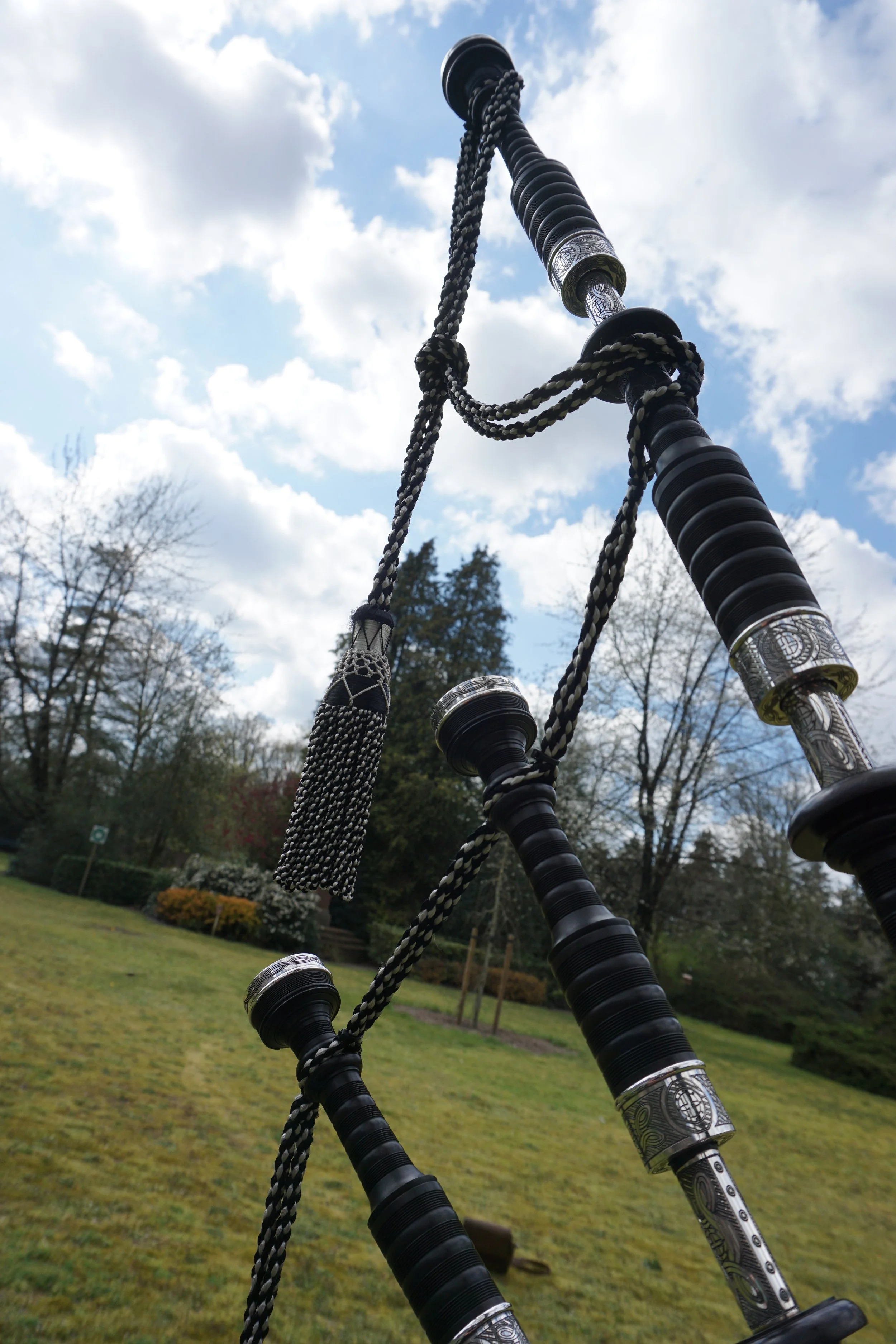 Een close-up van de drones van een doedelzak,  met een blauwe lucht en witte wolken op de achtergrond.