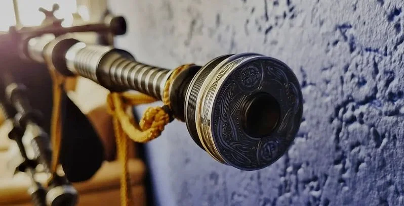 Close-up van een doedelzak bassdrone met een gedetailleerd, versierd eindstuk, bevestigd aan een muur.