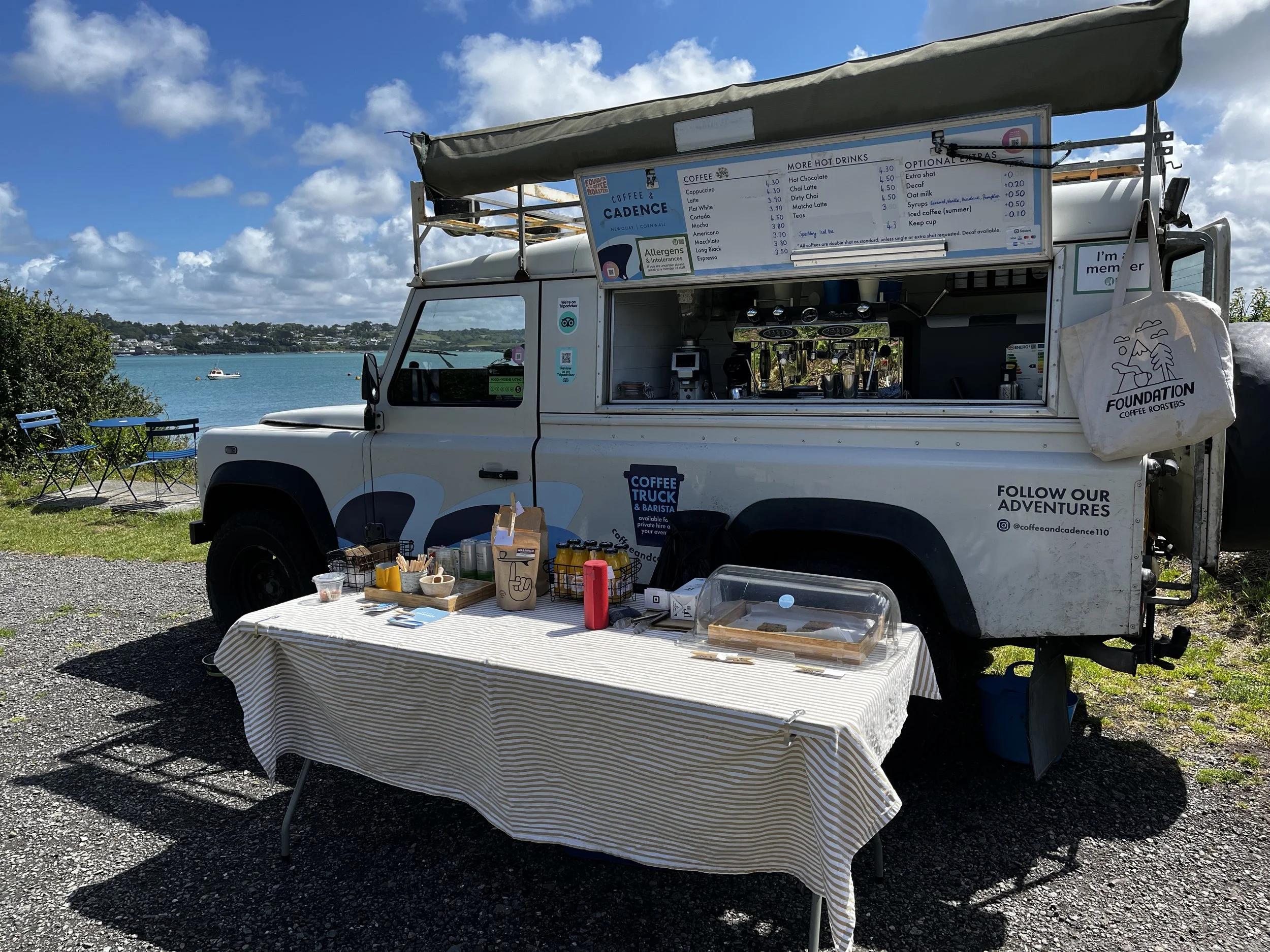 A white Land Rover Defender converted as a mobile coffee van on the Camel Trail in Padstow Cornwall with cakes and pastries displayed