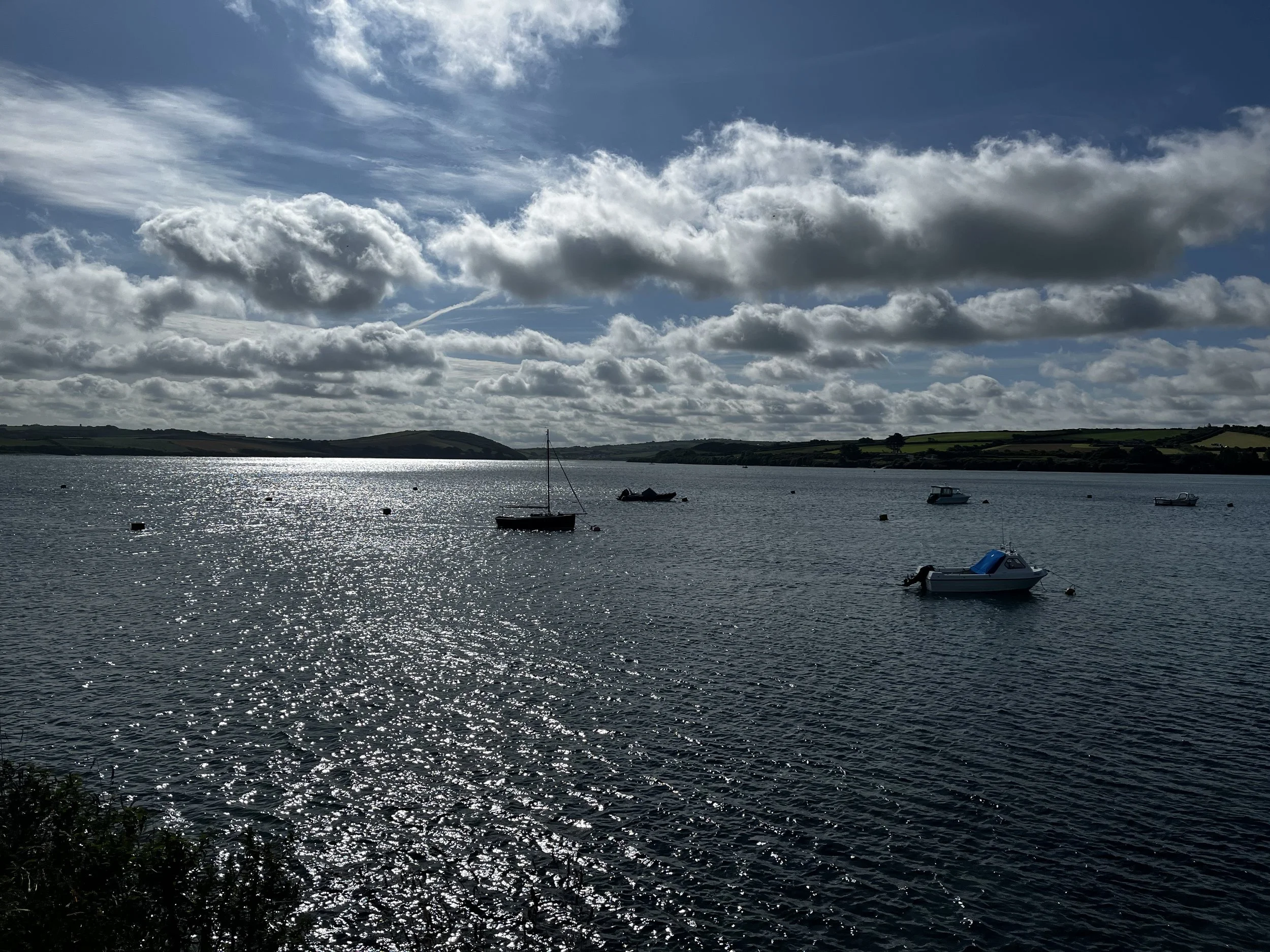 Boats floating on a calm body of water with a partly cloudy sky overhead and distant green hills.