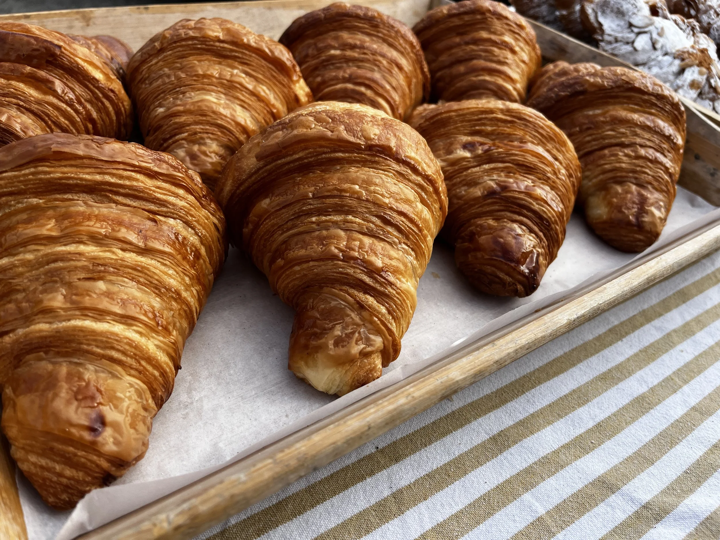 A tray of freshly baked croissants on white parchment paper, placed on a striped cloth surface.