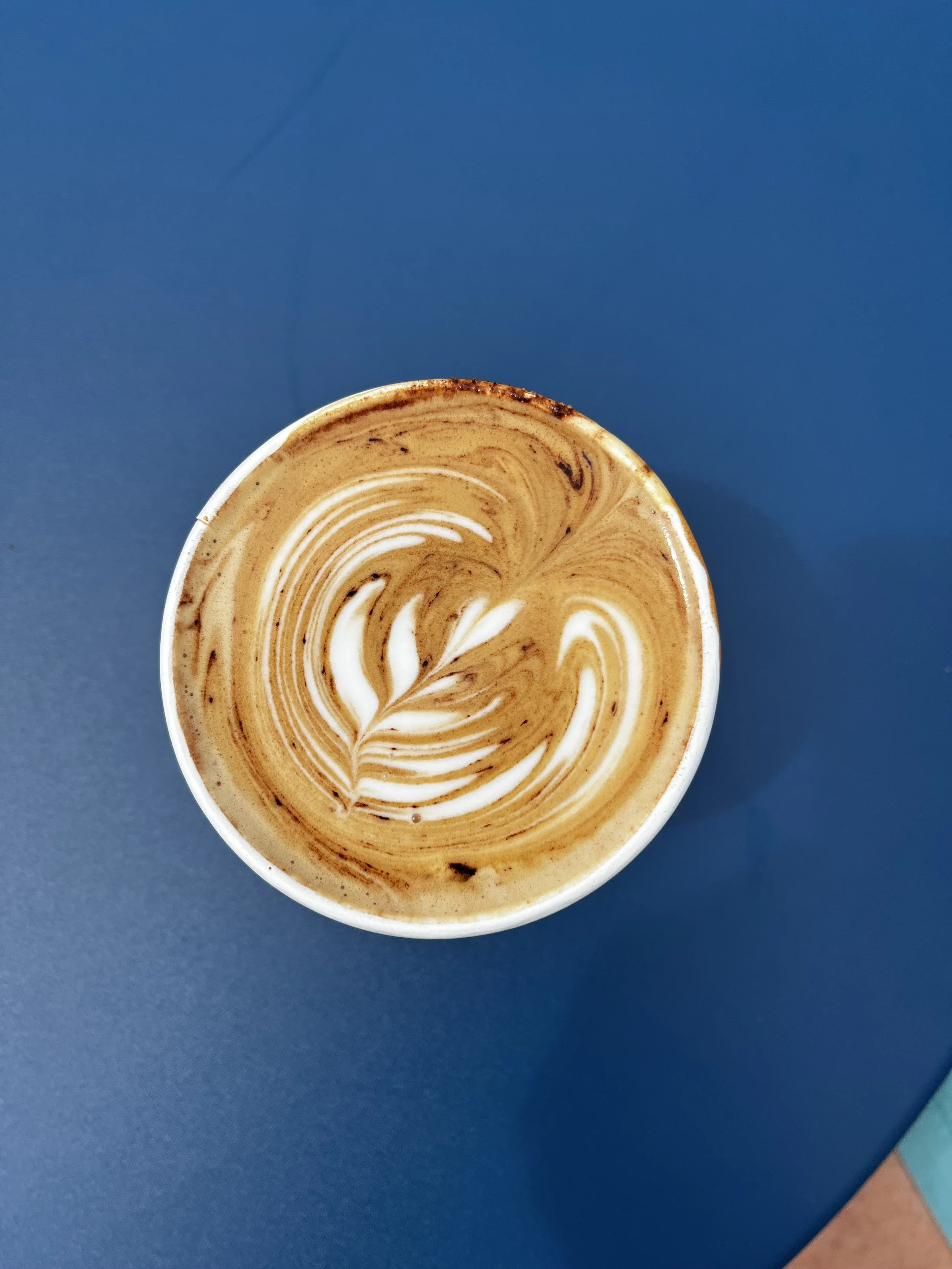 Top view of a cup of latte with latte art on a blue table.