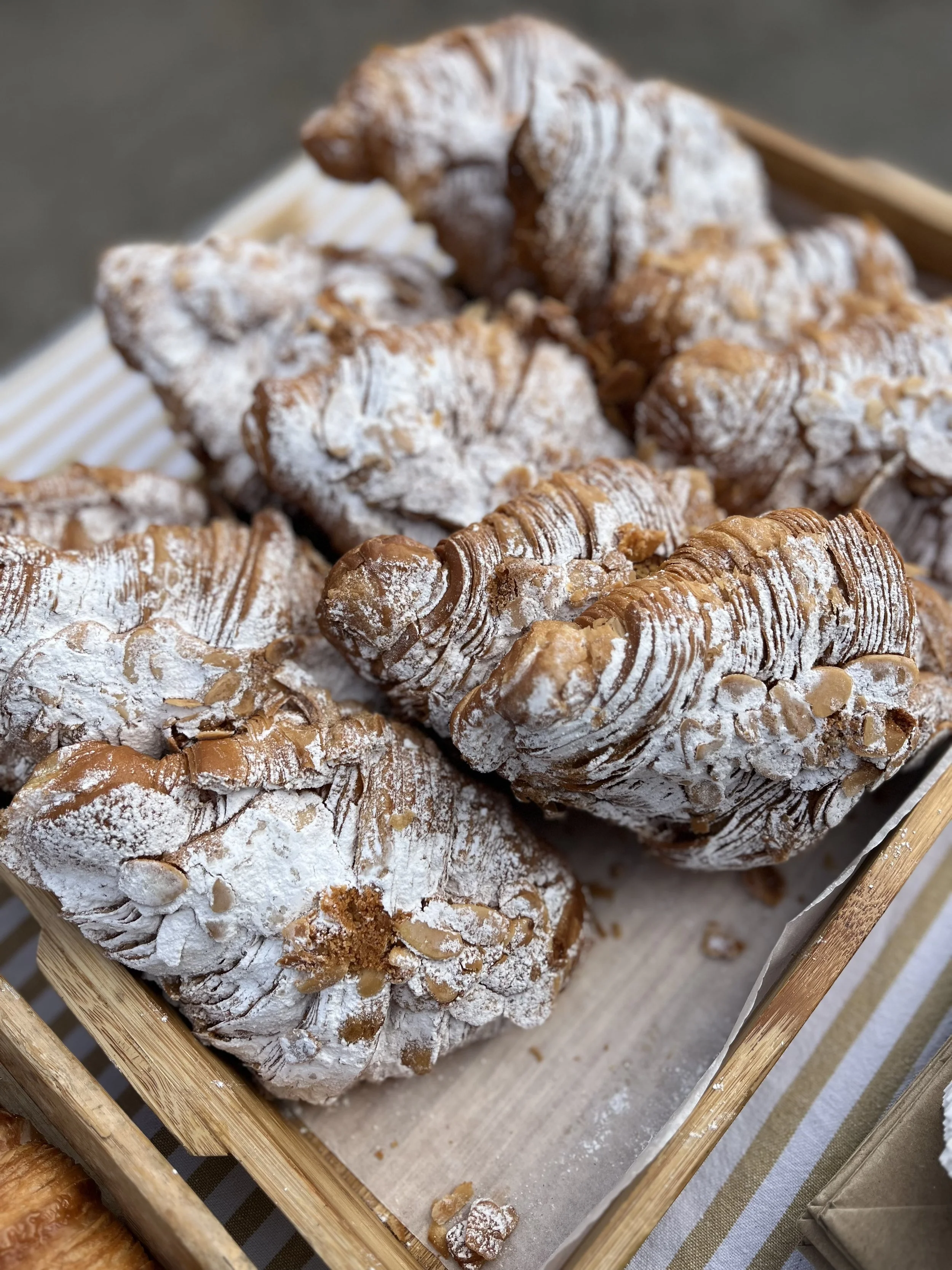 Assorted pastries covered in powdered sugar, displayed in a wooden tray.