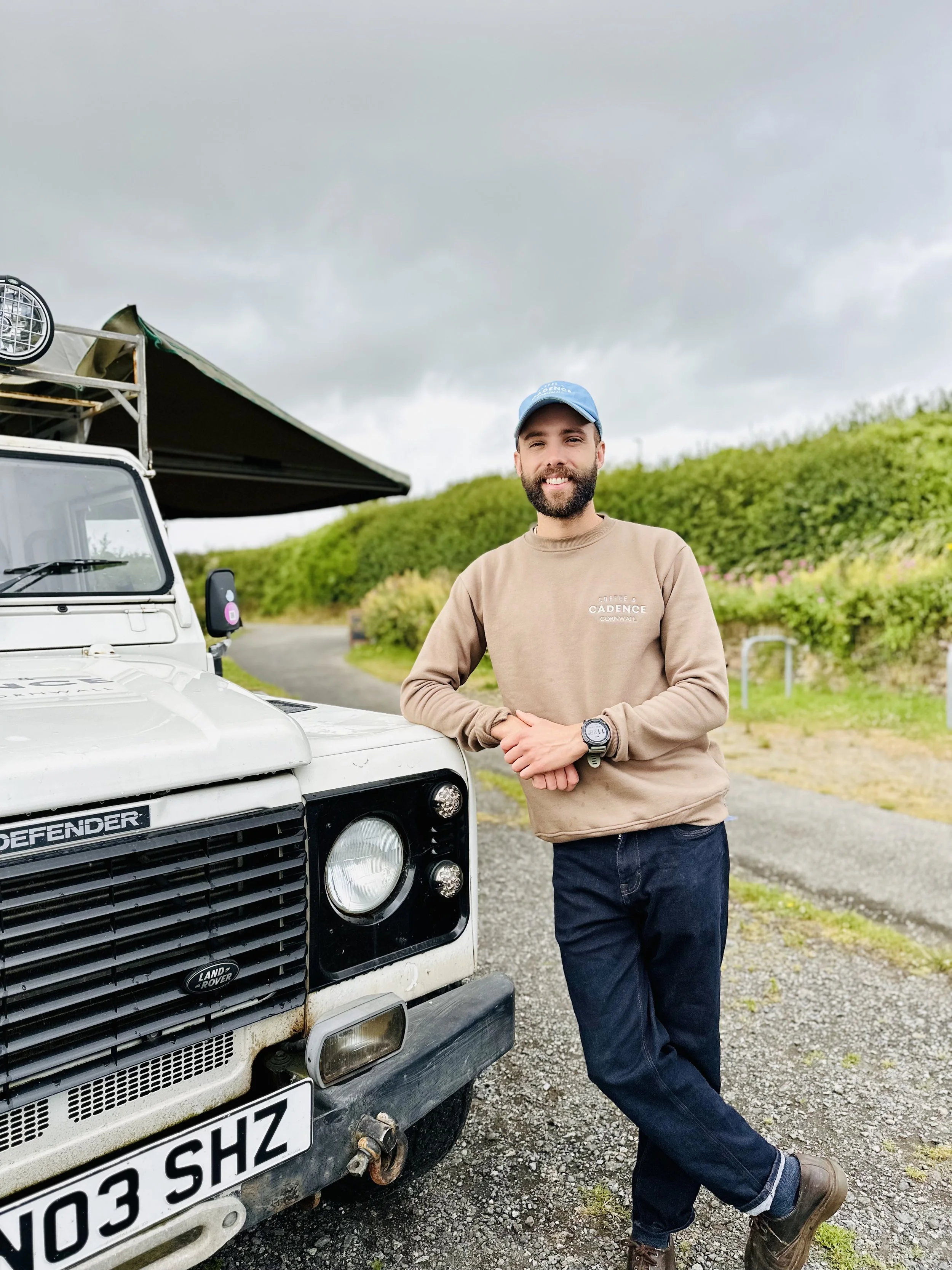 Owner of Coffee & Cadence leaning against the vintage Land Rover Defender mobile coffee truck in Cornwall.