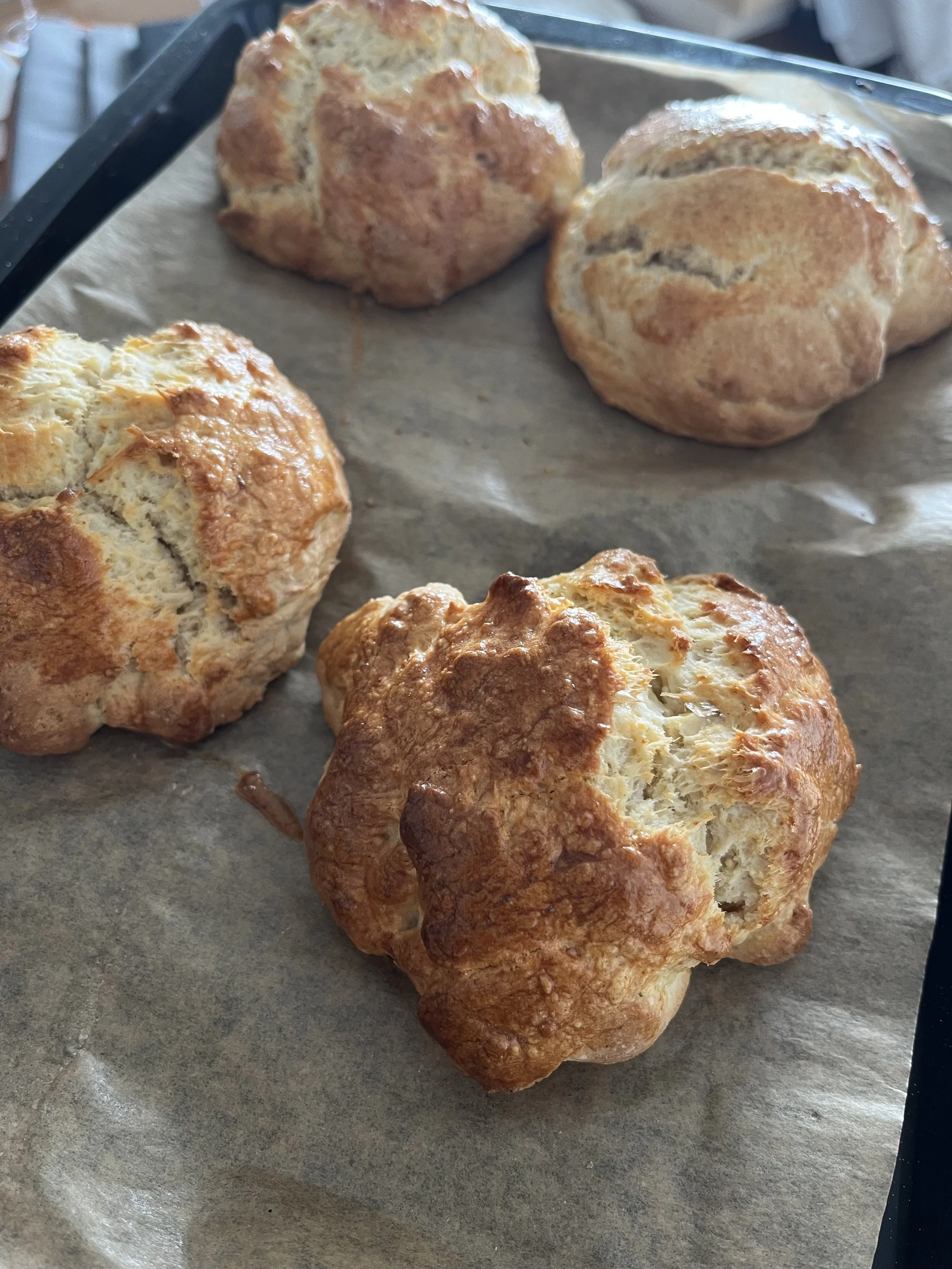 Four freshly baked scones on parchment paper, with a golden-brown, crusty exterior and a soft interior.