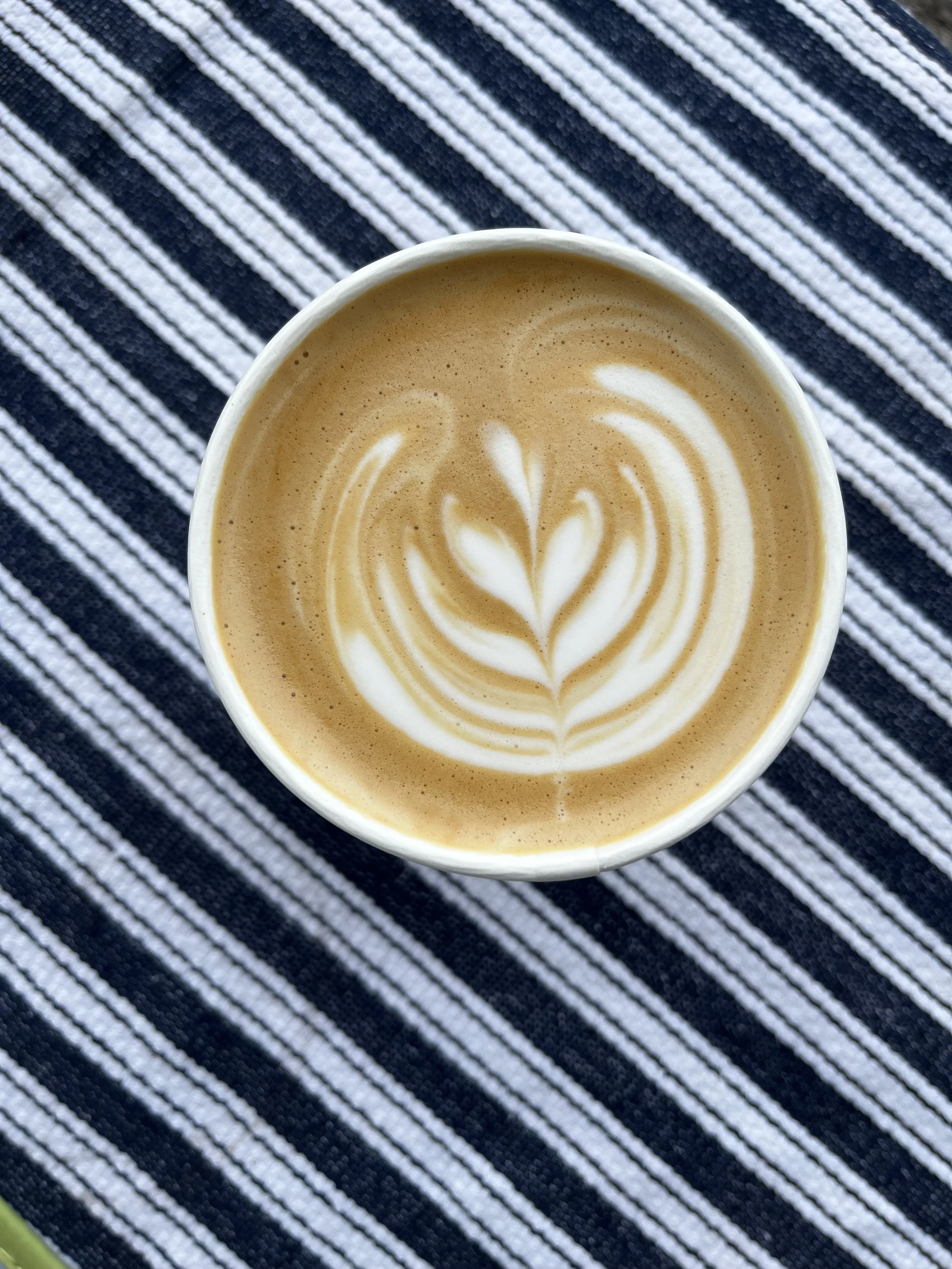 A cup of coffee with latte art in a stripe pattern background.