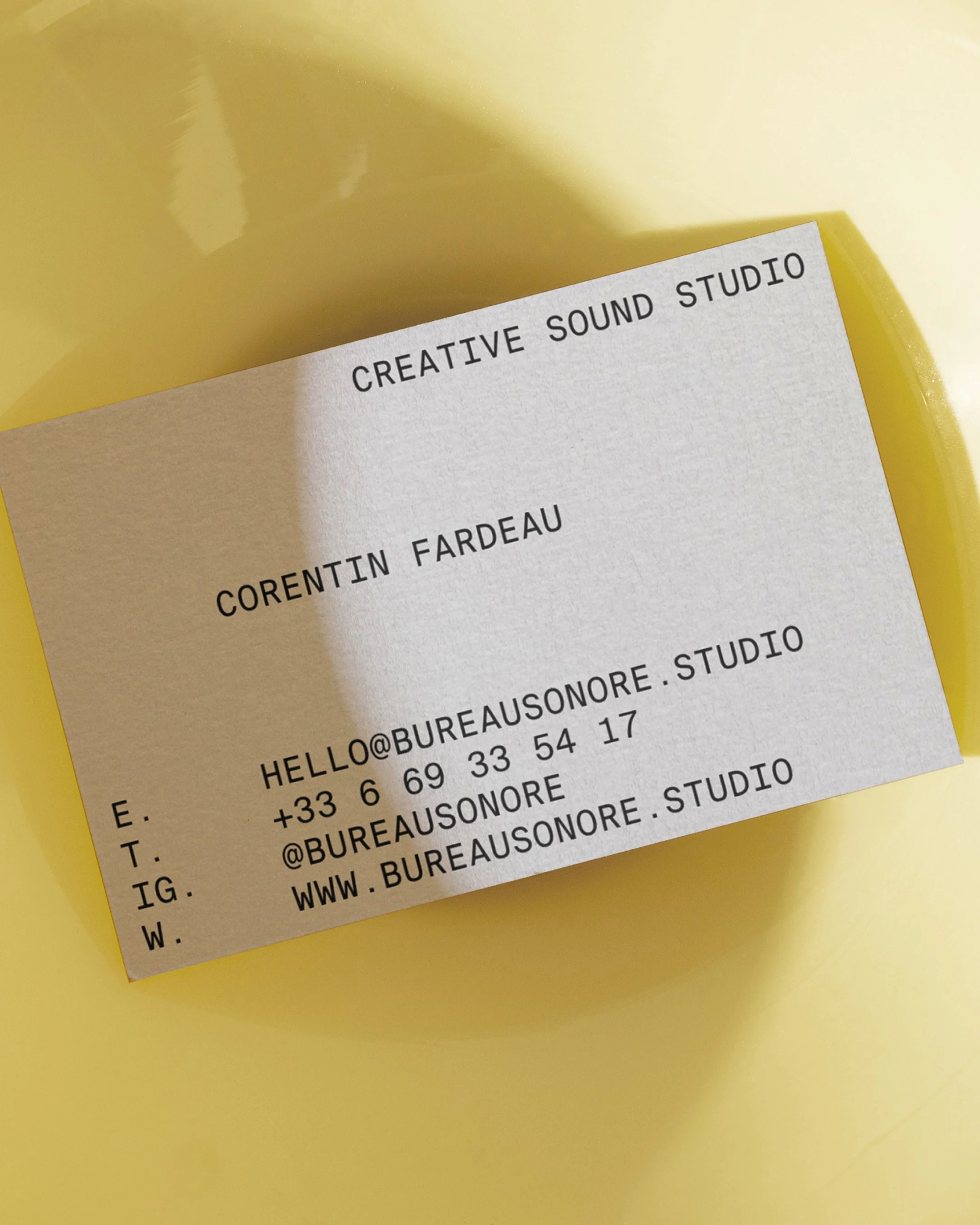 Carte de visite blanche avec texte noir, incluant le nom Corentin Fardeau et les coordonnées, posée sur un fond jaune.