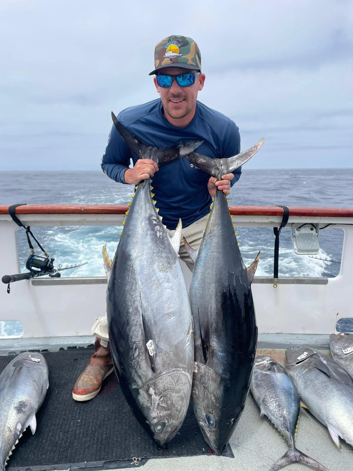 Man holding two large tuna fish on a boat at sea.