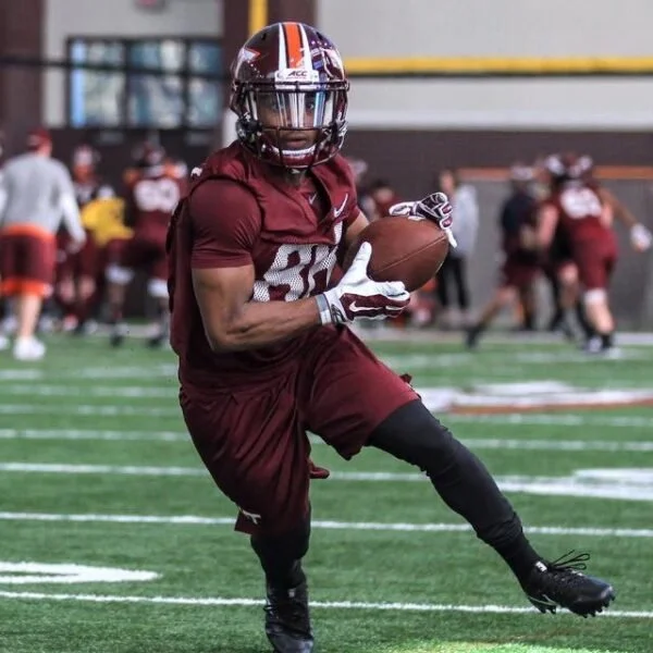 A football player in a maroon uniform practicing with a football on a field during a game or training session.