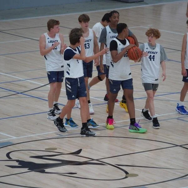 Group of young boys in basketball uniforms on an indoor court, with one holding a basketball.